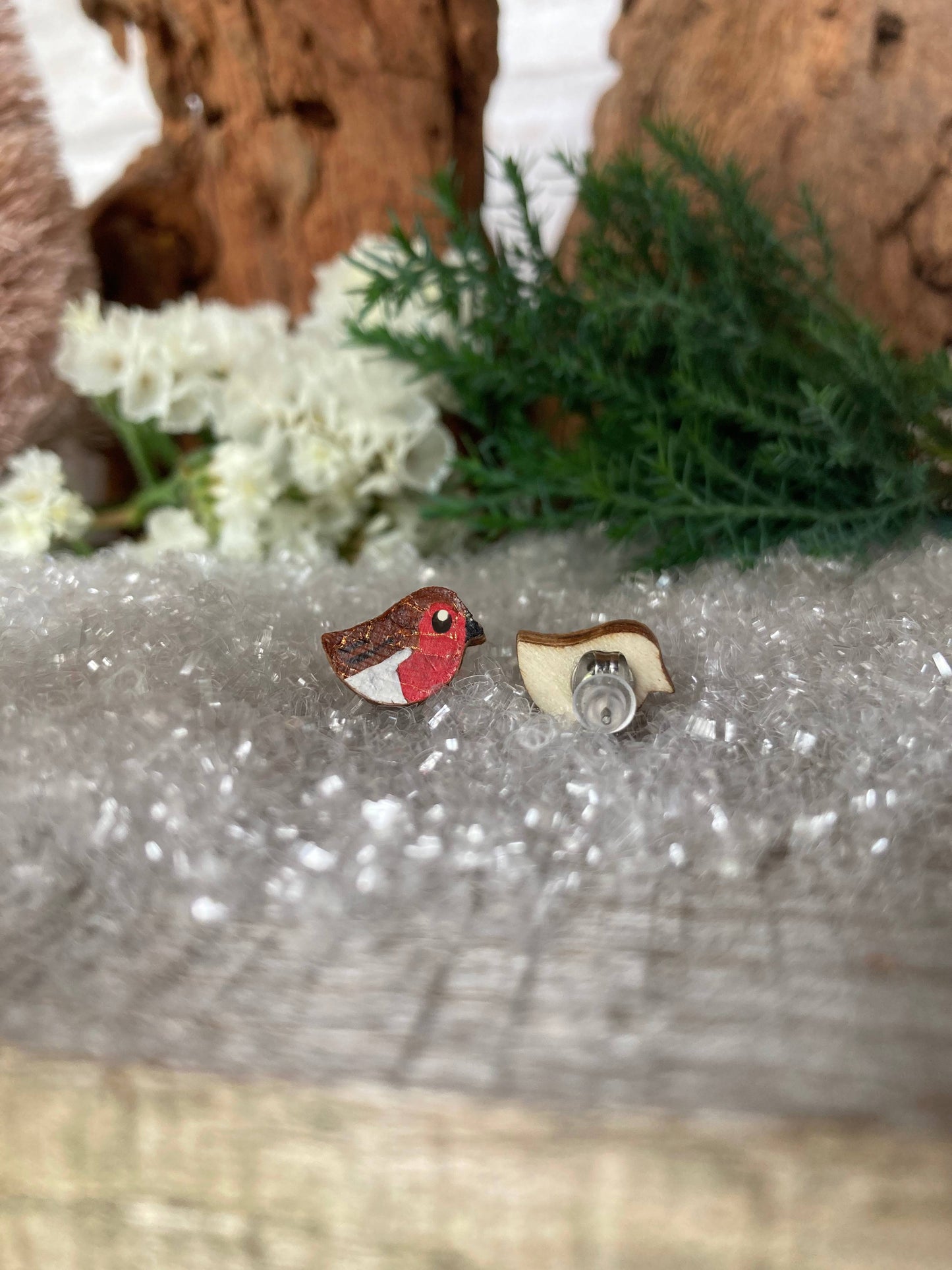 Pair of bird-shaped earrings on a textured surface with flowers and wood in the background