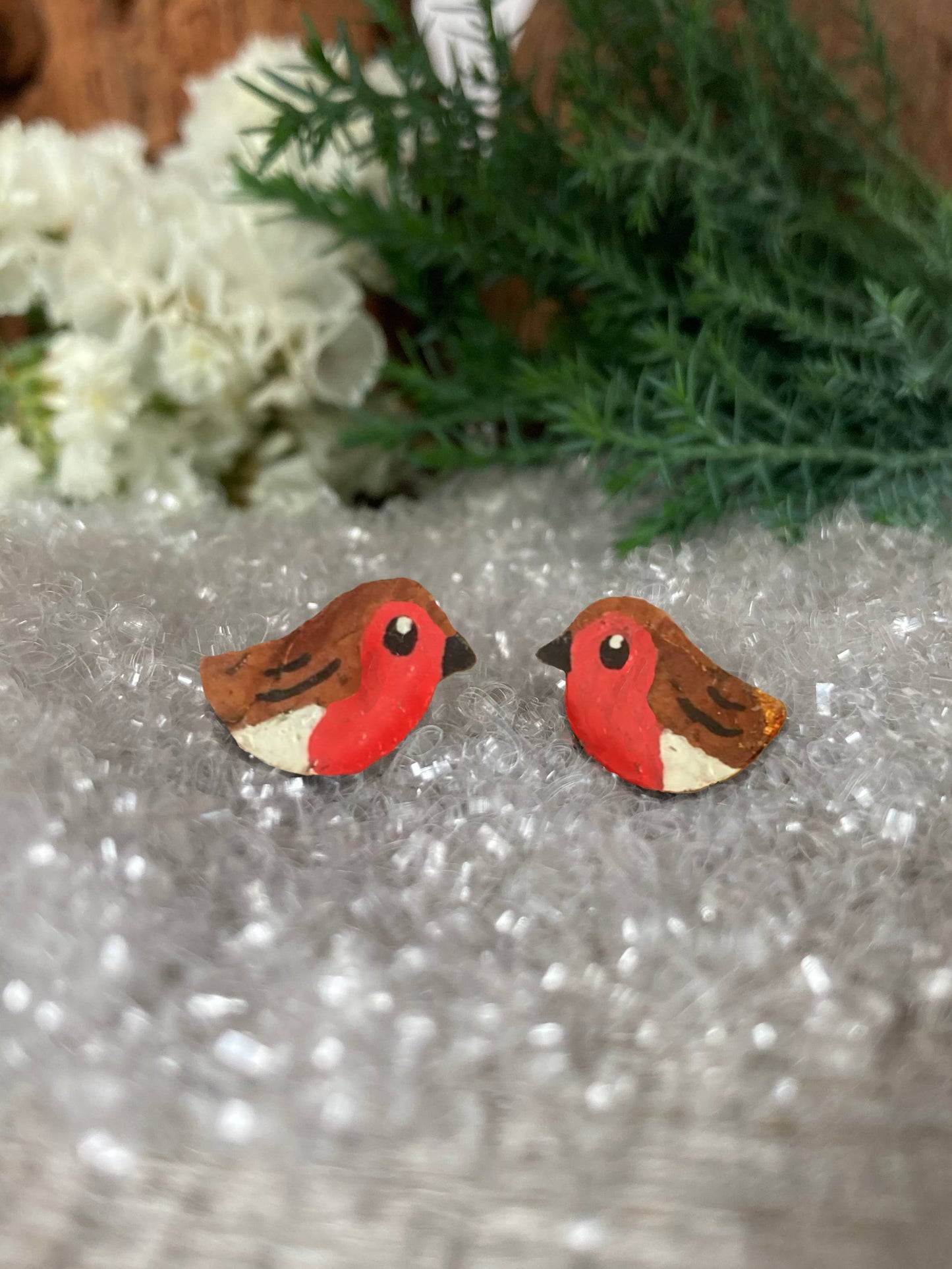 Pair of robin-shaped earrings on a textured surface with greenery in the background
