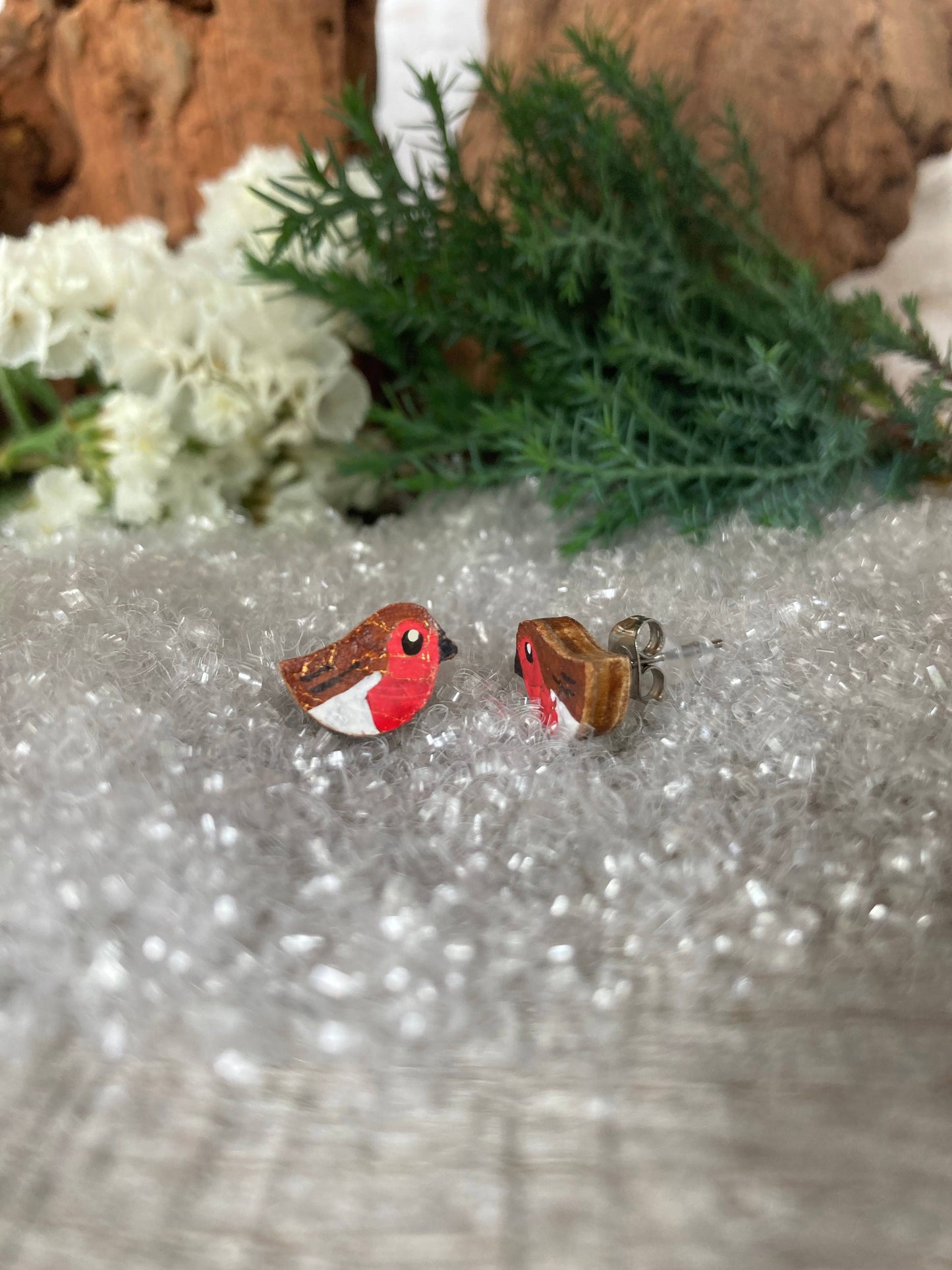 Bird-shaped earrings on a textured surface with greenery and flowers in the background