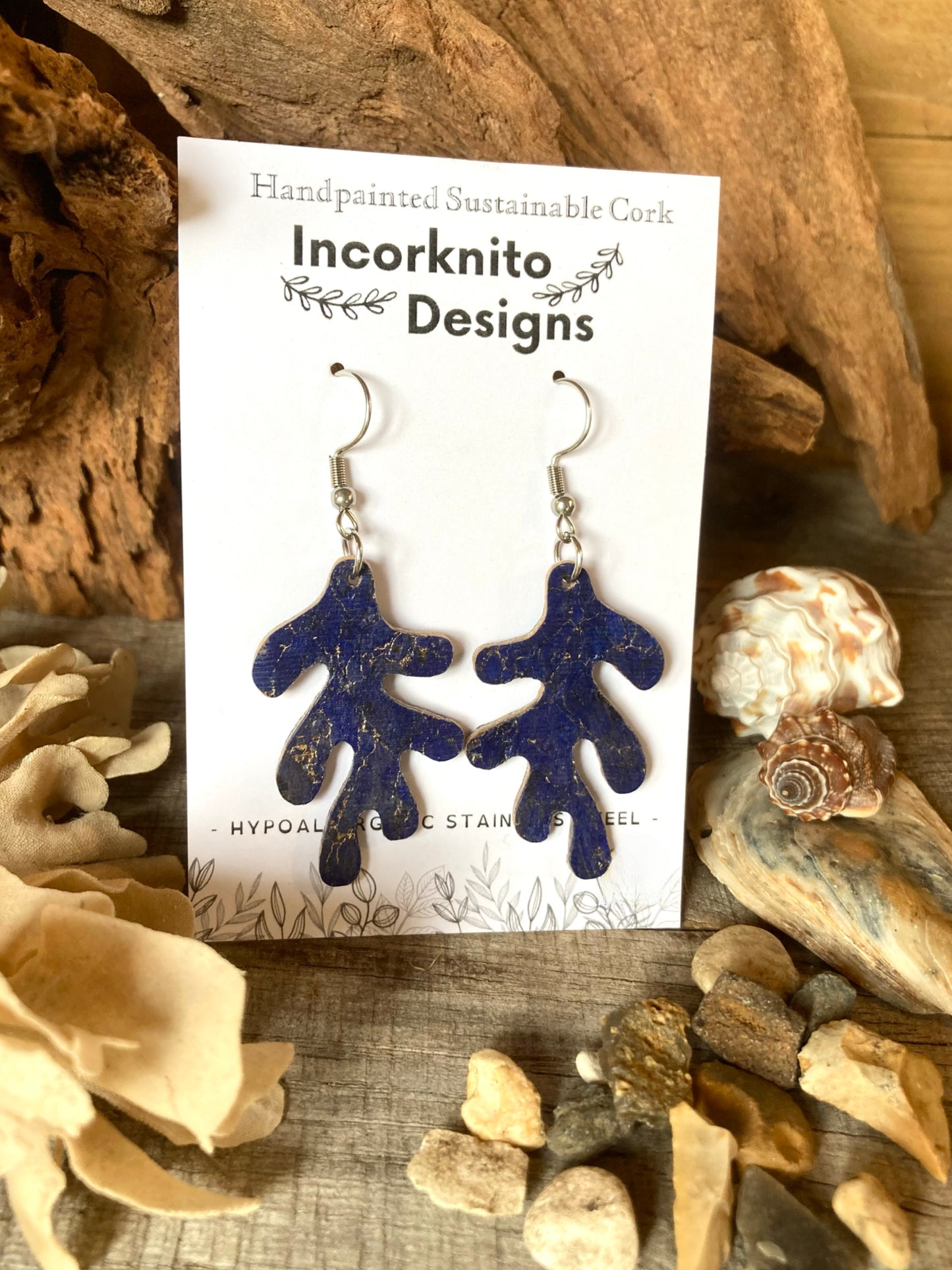 Blue coral-shaped earrings on a card with 'Incorknito Designs' branding, surrounded by natural elements.