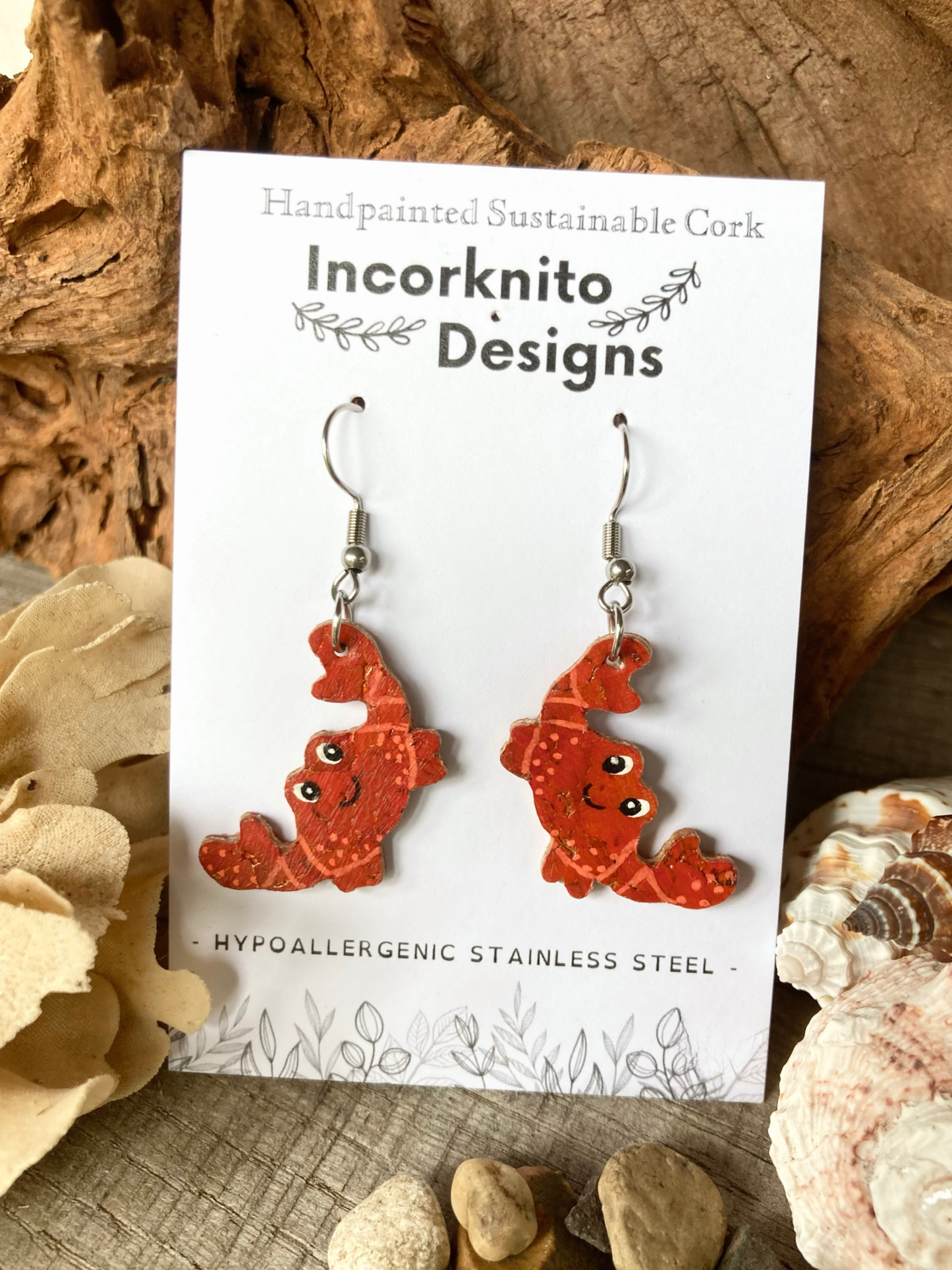Orange crab-shaped earrings on a 'Incorknito Designs' card with natural elements in the background.