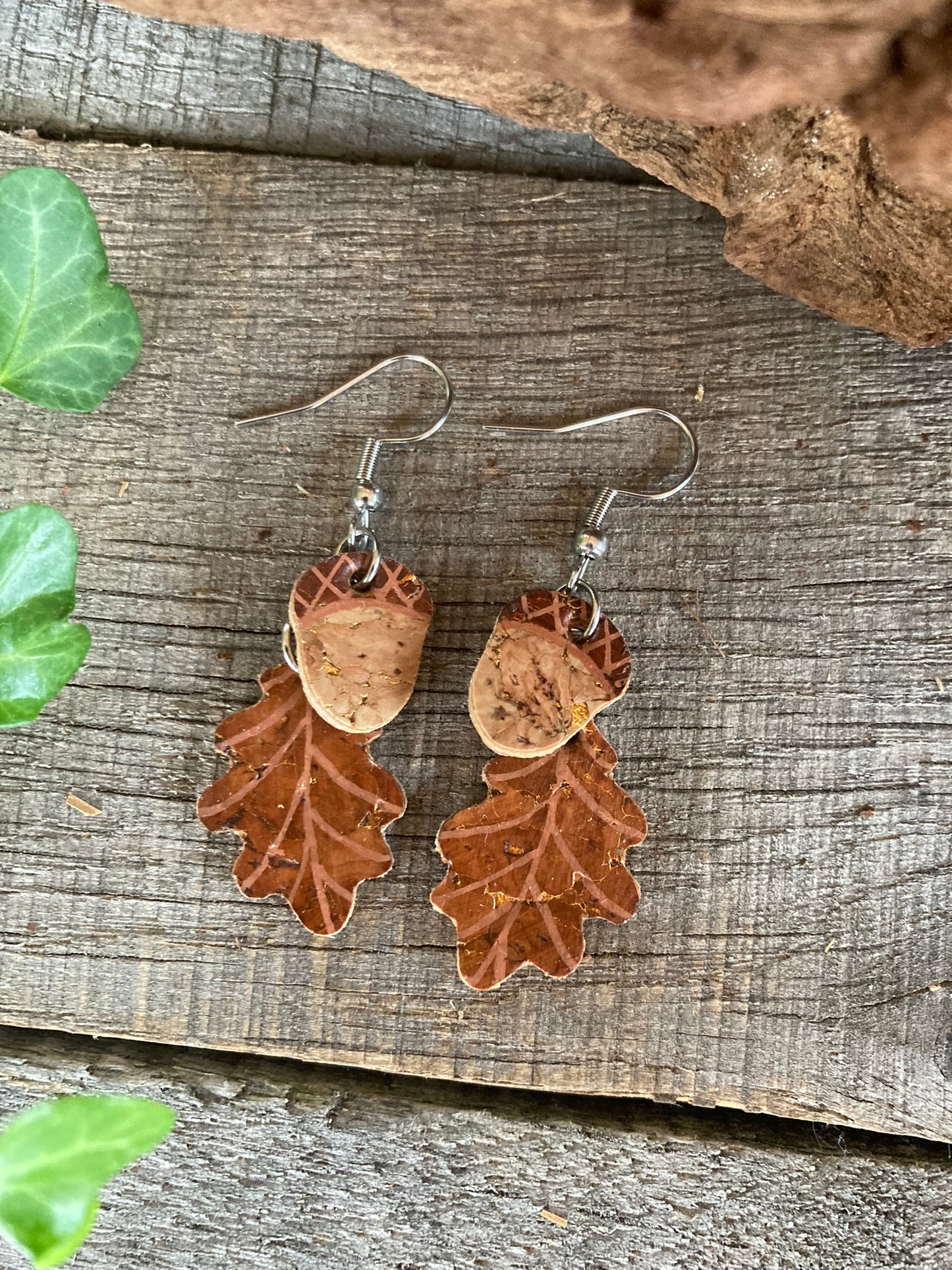Pair of cork earrings in the shape of an acorn and oak leaf placed on a wooden background