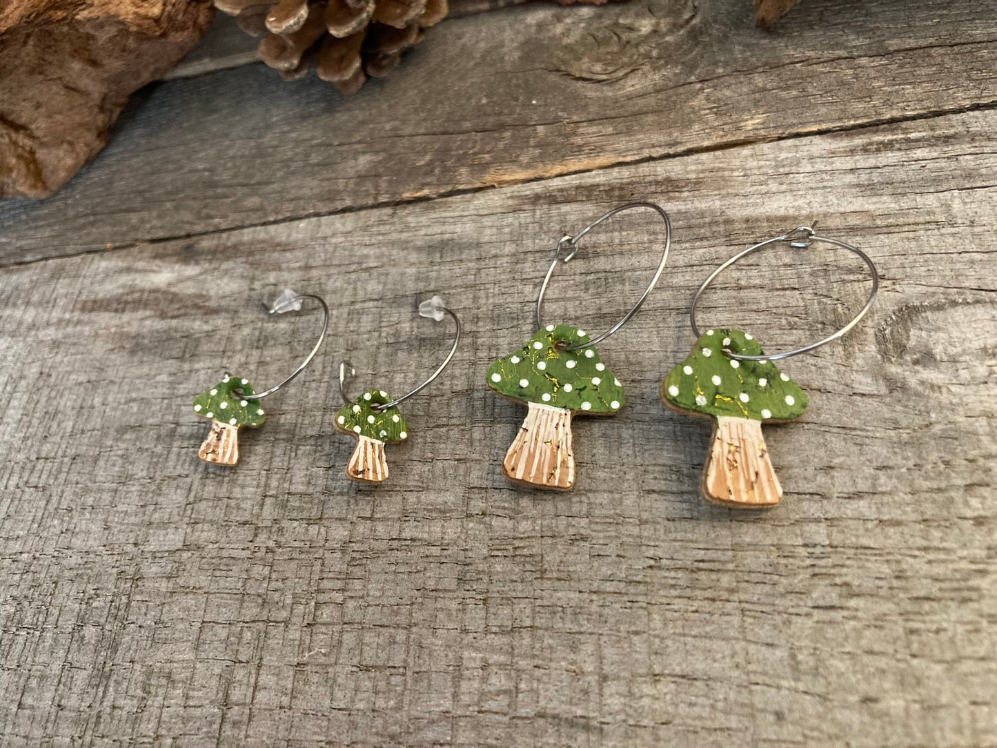 Mini and large green polka dot toadstool earrings on a wooden surface