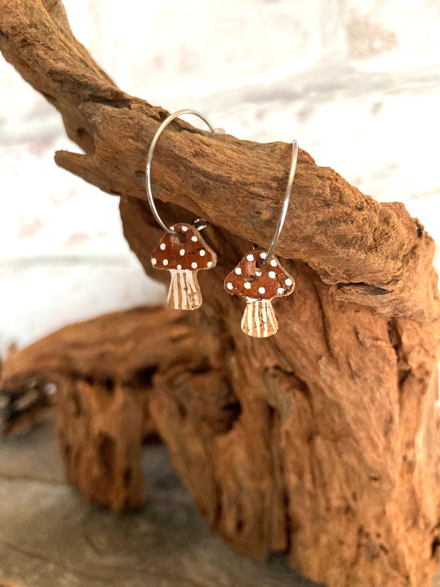 Mini brown toadstool hoop earrings perched on a wooden branch