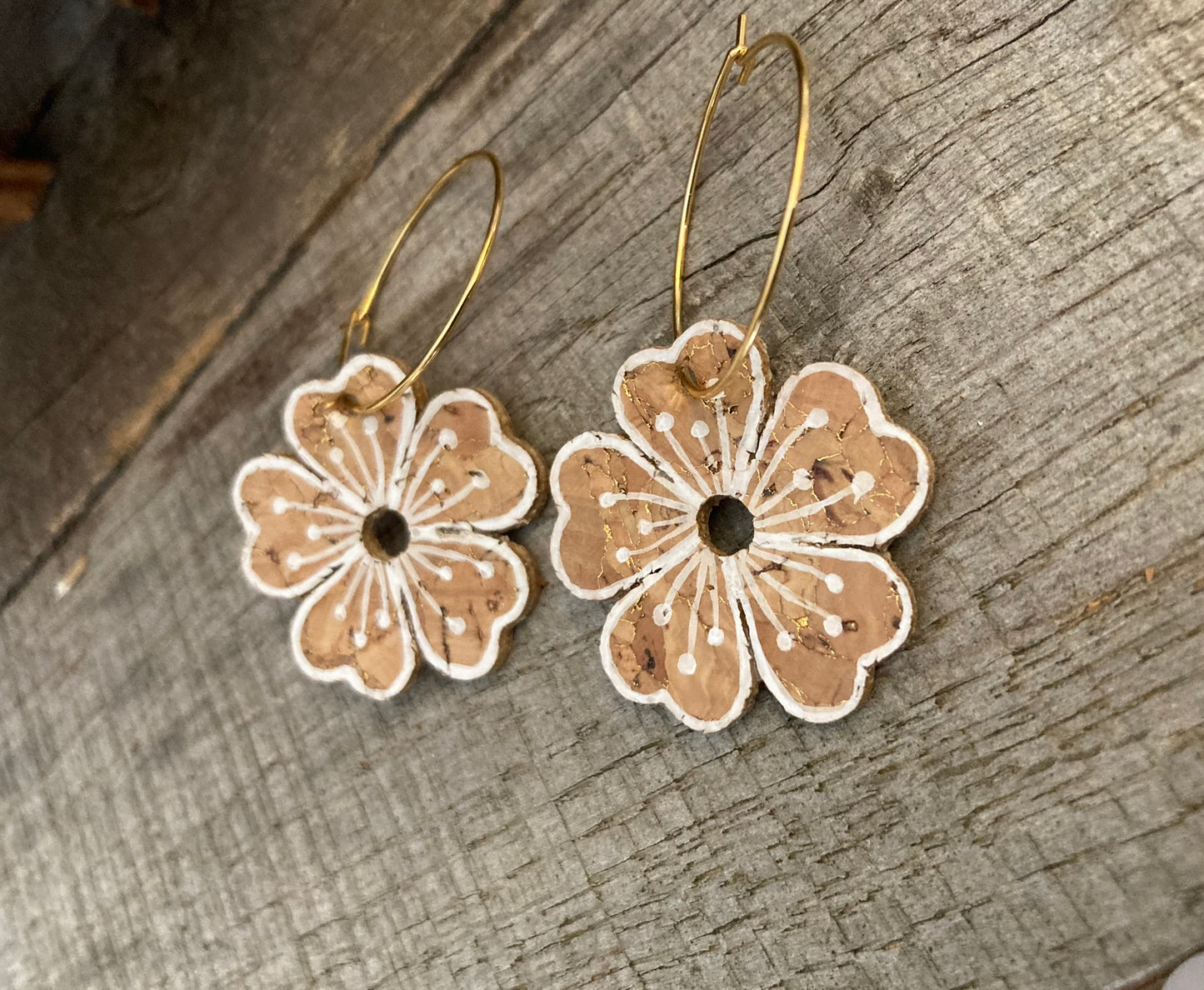Natural cork flower earrings with white detailing on a wooden backgorund