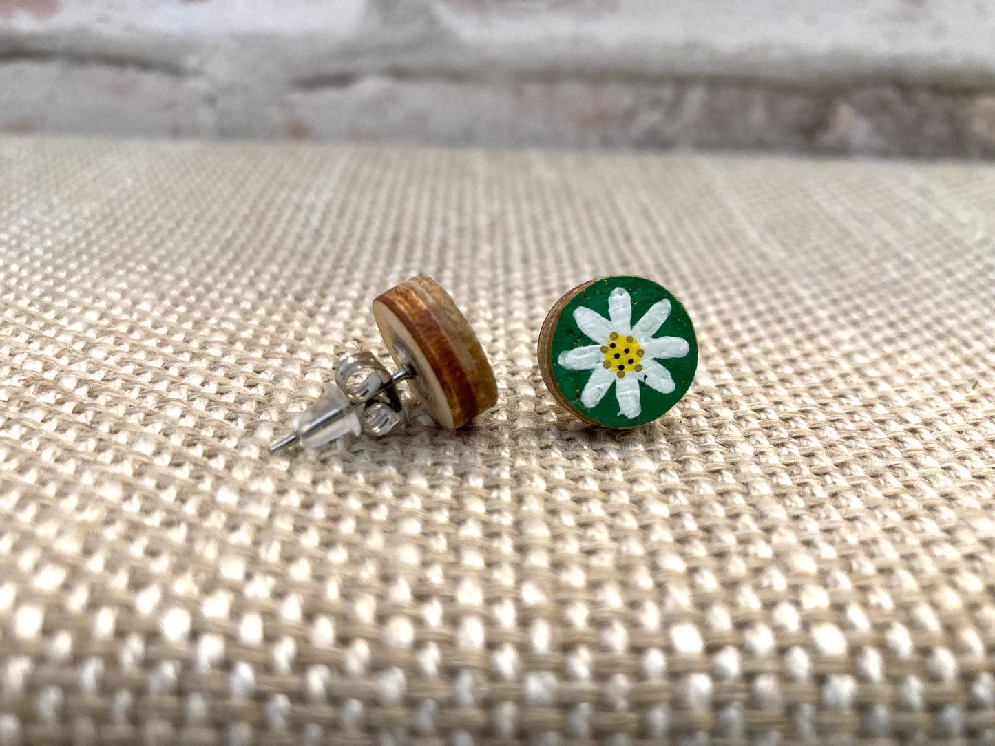 Khaki daisy earring studs showing the side view and natural wood backs on a woven material surface