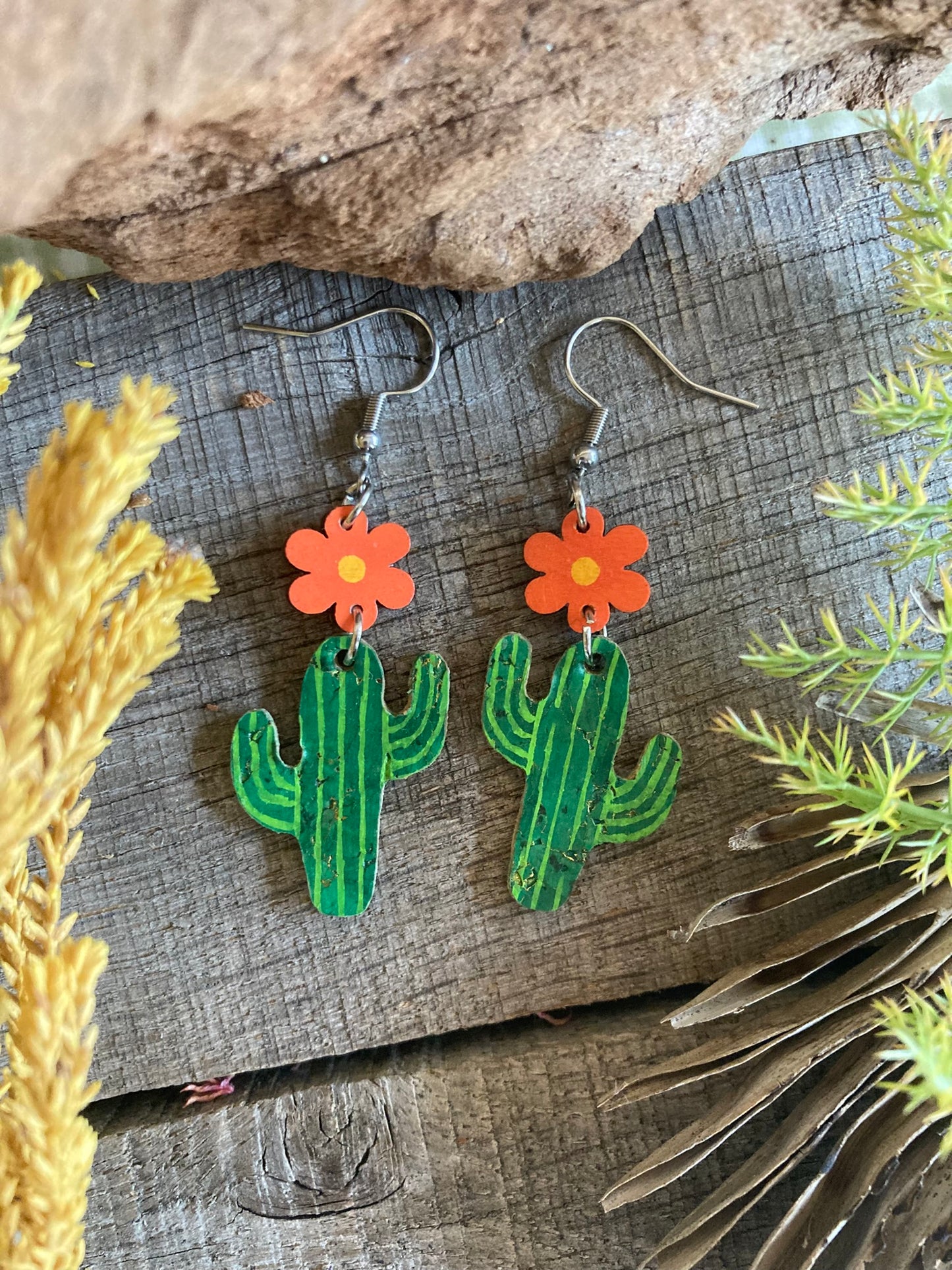 Cactus-shaped earrings with orange flowers on a wooden surface.