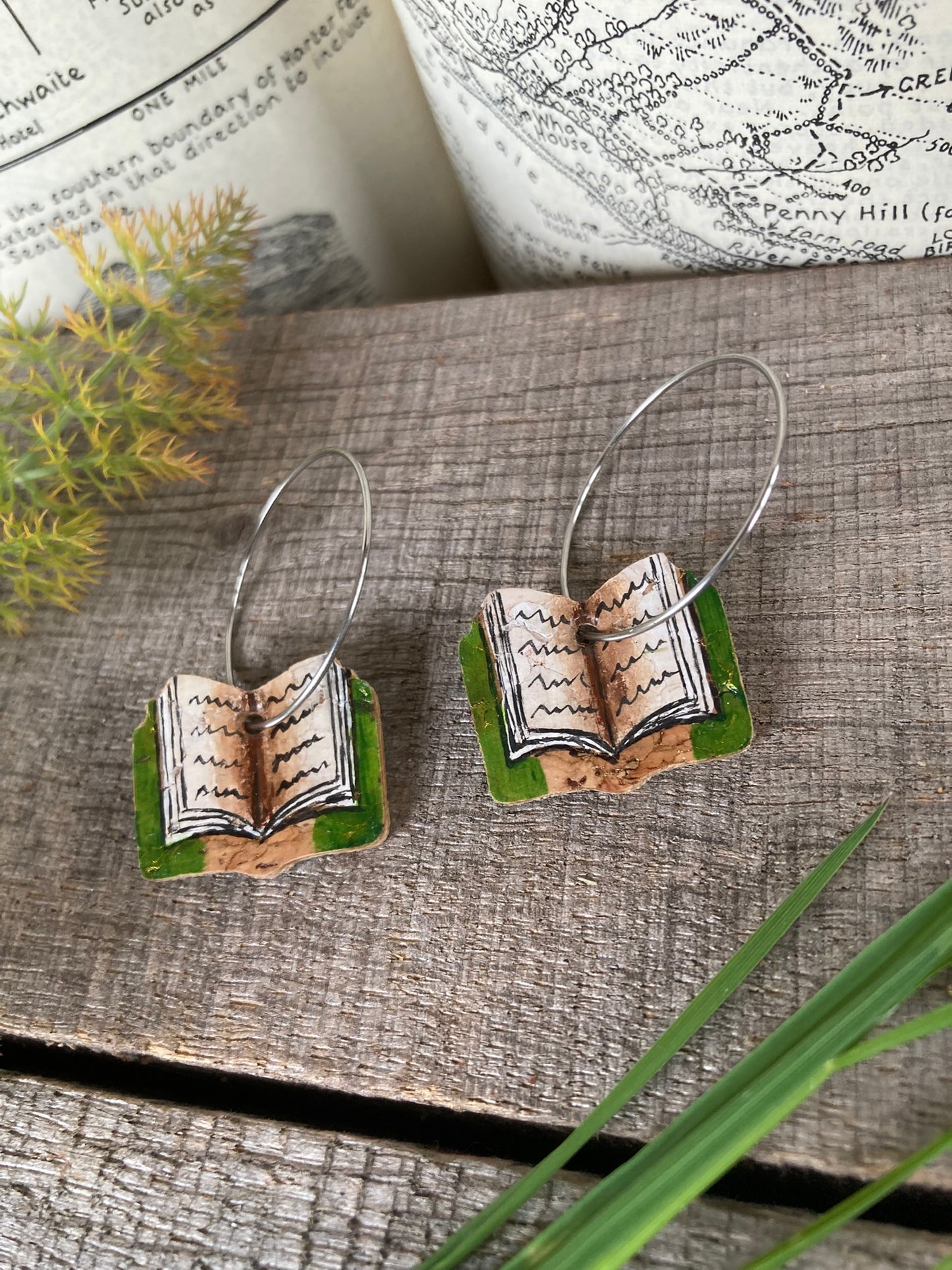 Book-shaped earrings on a textured surface with an open book in the background