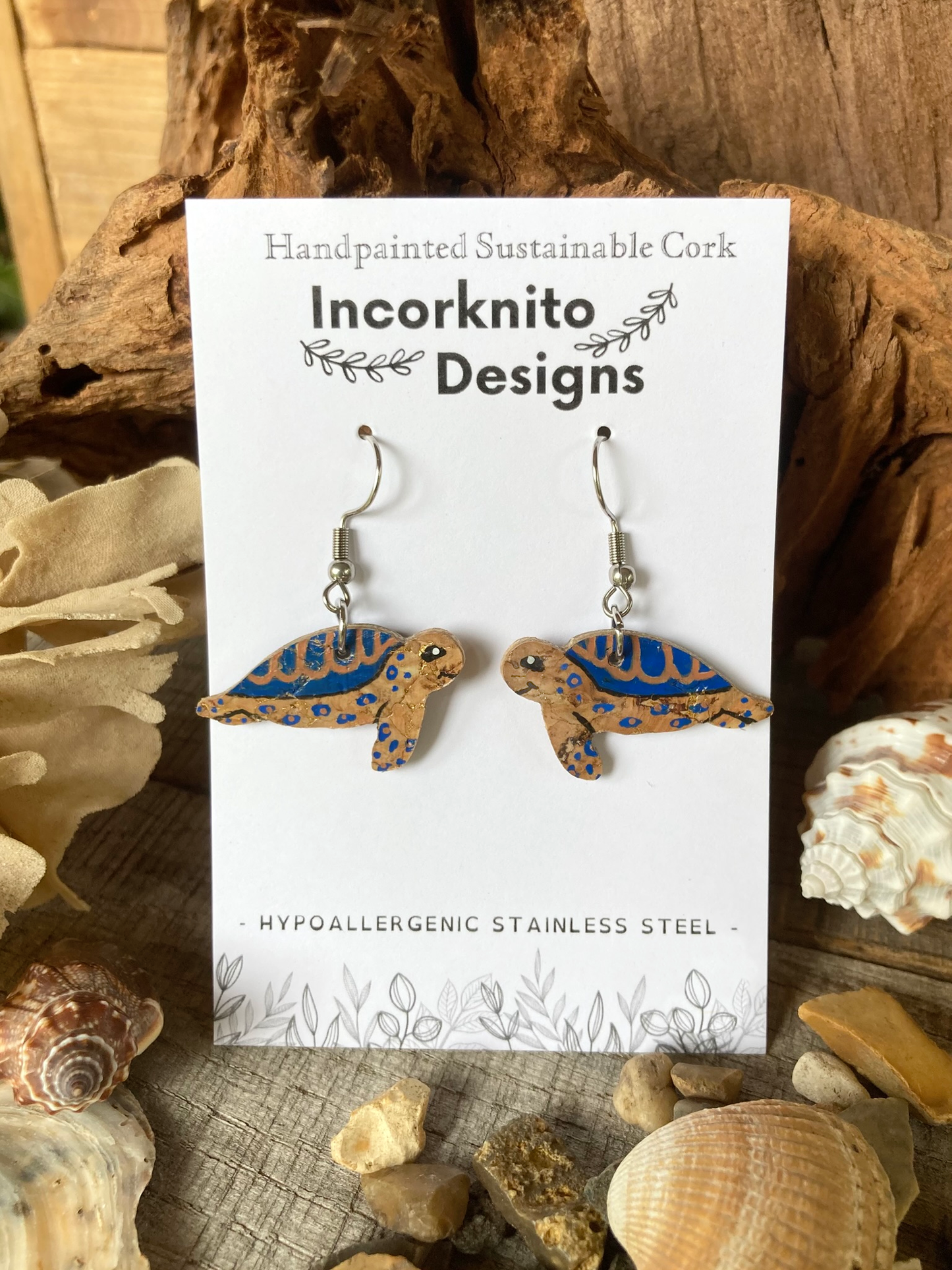 Turtle-shaped earrings on a card with 'Incorknito Designs' branding, surrounded by natural elements.