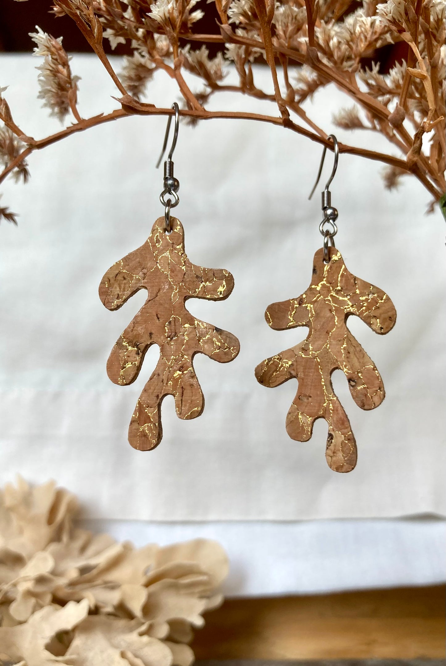 Gold flecked cork abstract leaf shaped earrings on a white background with dried flowers.
