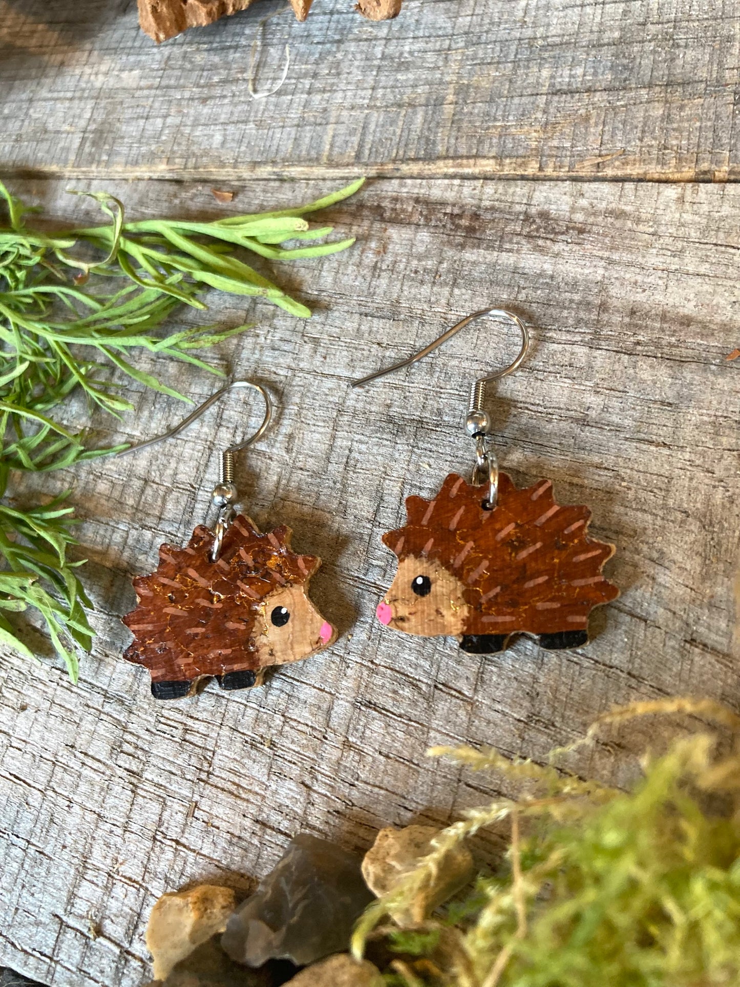 Hedgehog-shaped earrings on a wooden surface with greenery