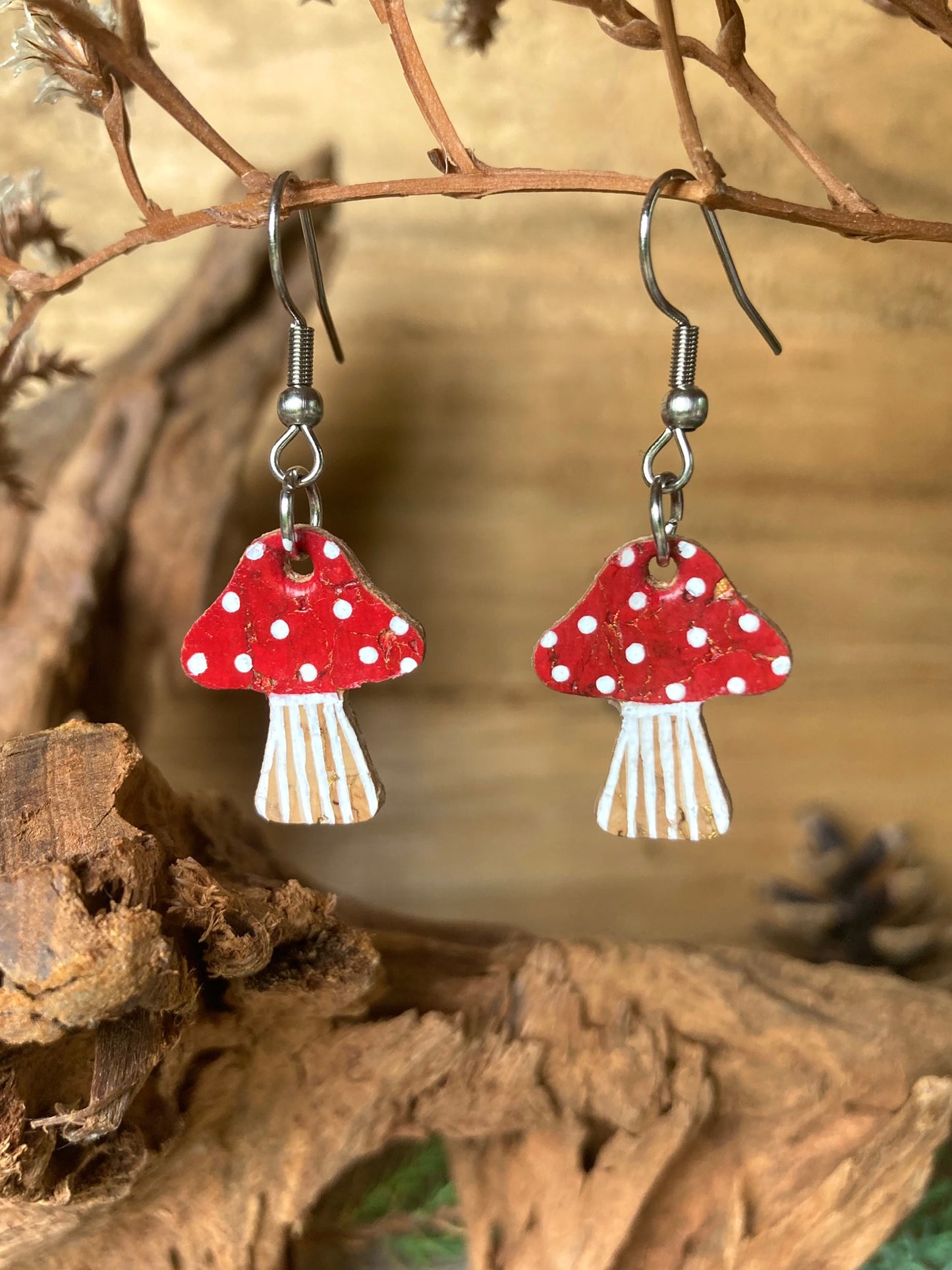 Red toadstool-shaped earrings with white polka dot design hanging on a branch.