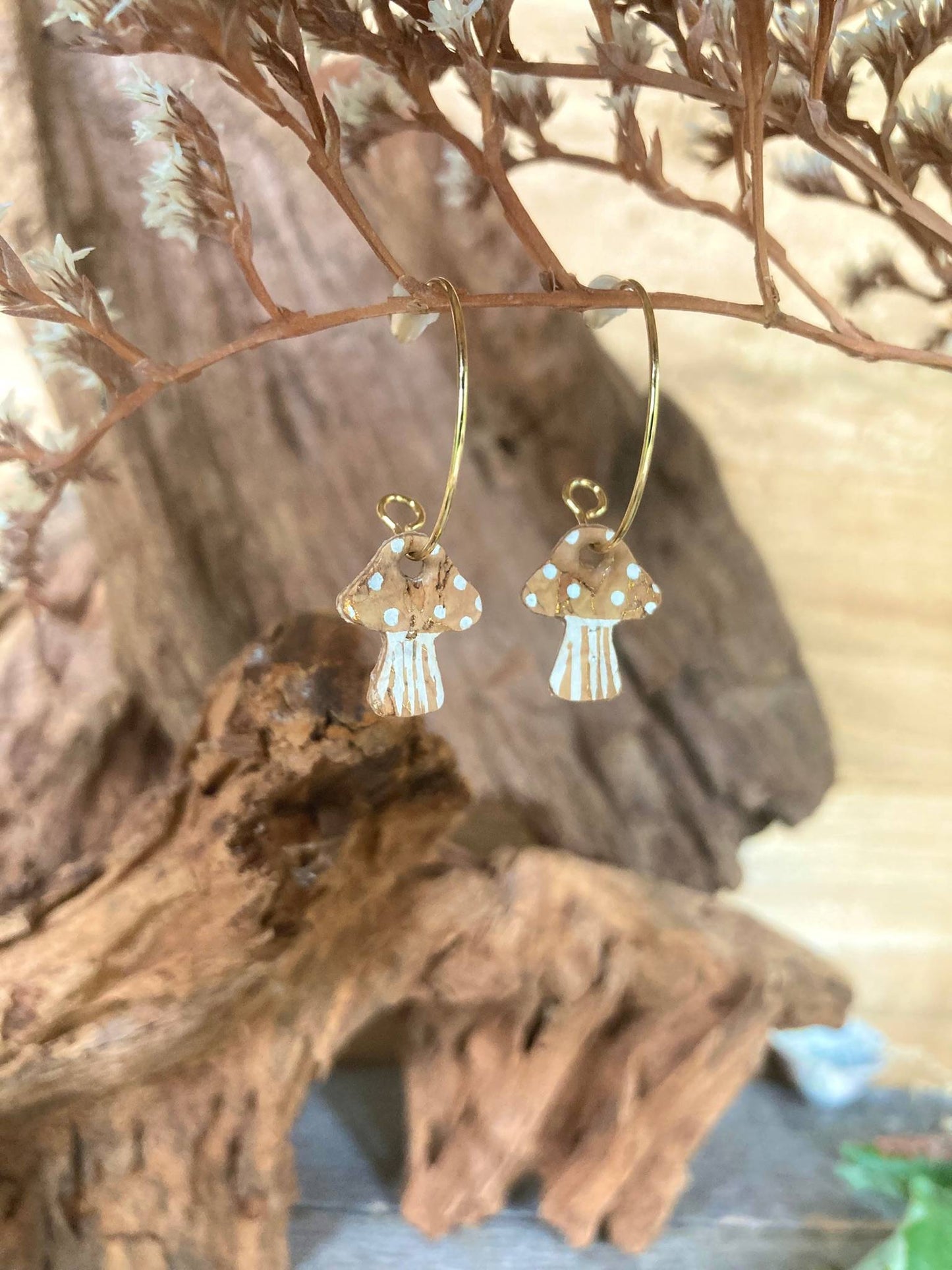 Gold mushroom earrings with a spotted design on a wooden surface