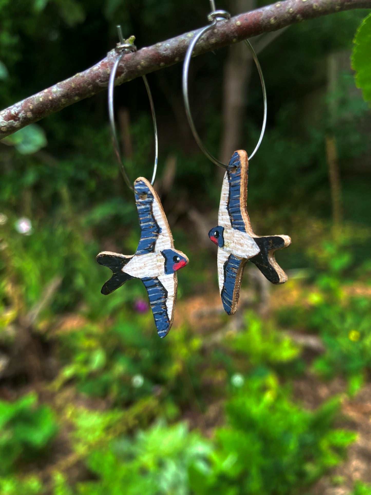Pair of bird-shaped earrings hanging on a branch with a natural green background