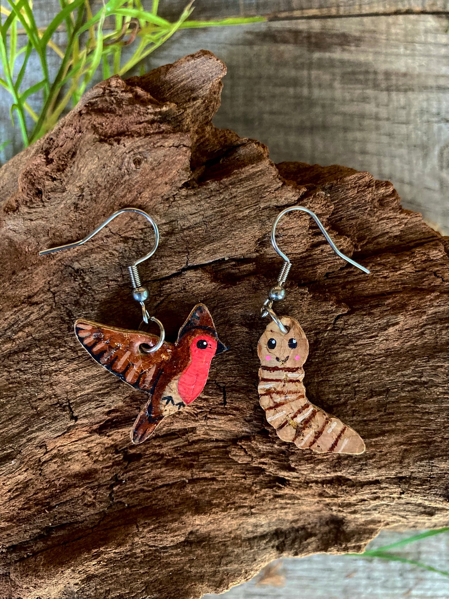 Pair of earrings shaped like a robin and a worm on a wooden surface.