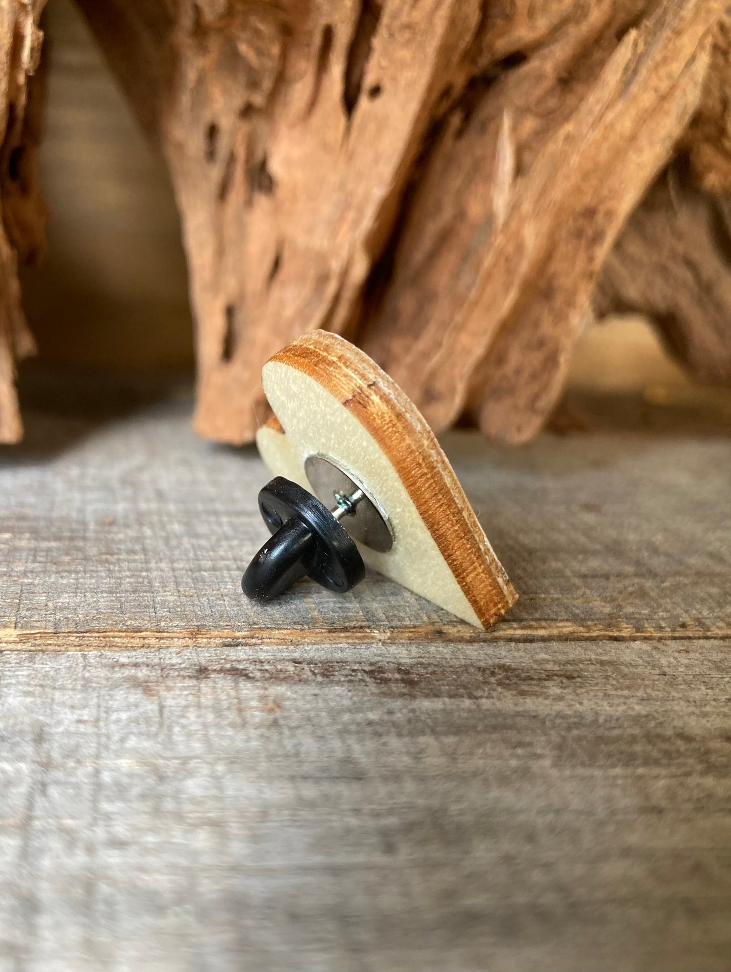 Small wooden pin badge with a black rubber back on a wooden surface