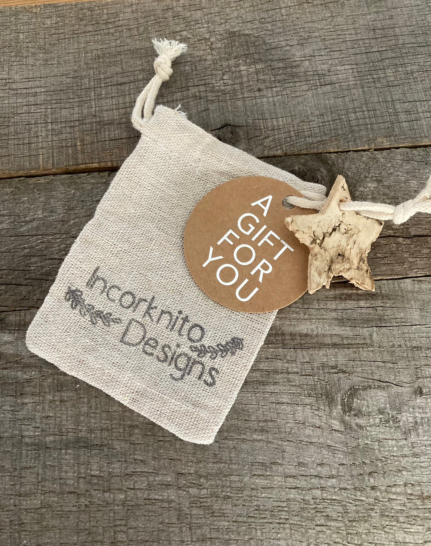 Incorknito Designs branded hessian drawstring gift bag with kraft gift tag and natural bark star charm on weathered wood