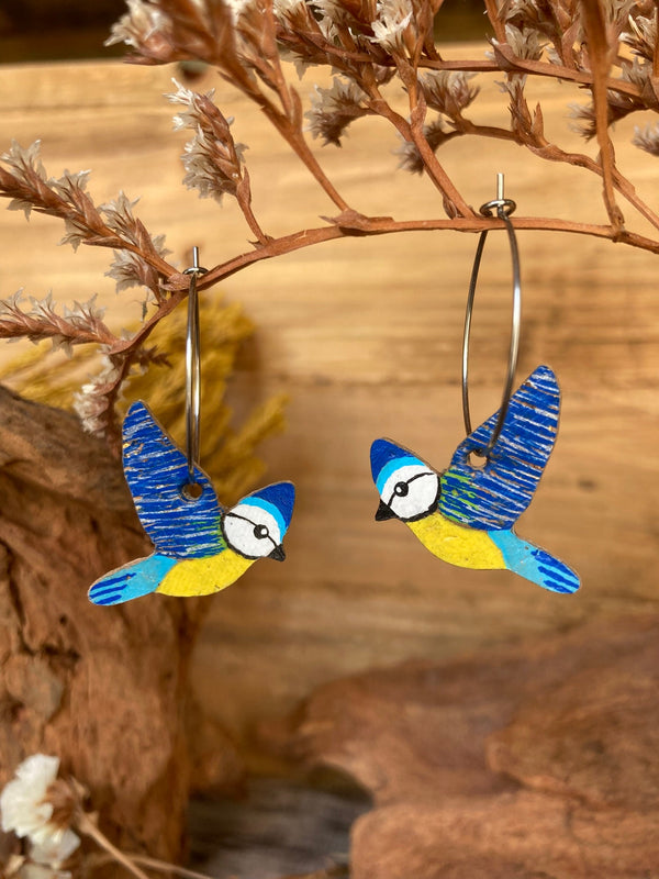 Bird-shaped earrings hanging on a branch with a natural background