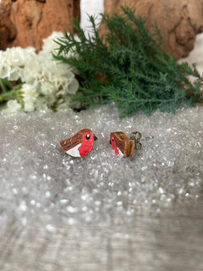 Bird-shaped earrings on a textured surface with greenery and flowers in the background