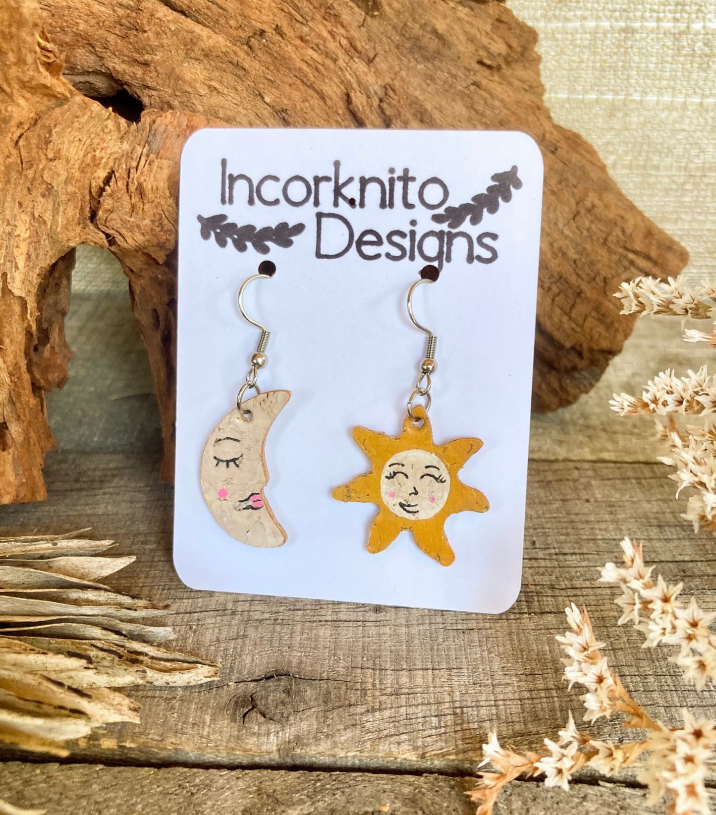 Sun and Moon cork earrings, a sustainable accessory choice. The earrings exhibit a celestial design, with a smiling sun on one side and a crescent moon on the other. Crafted from eco-friendly cork, these earrings radiate charm and nature-inspired style.