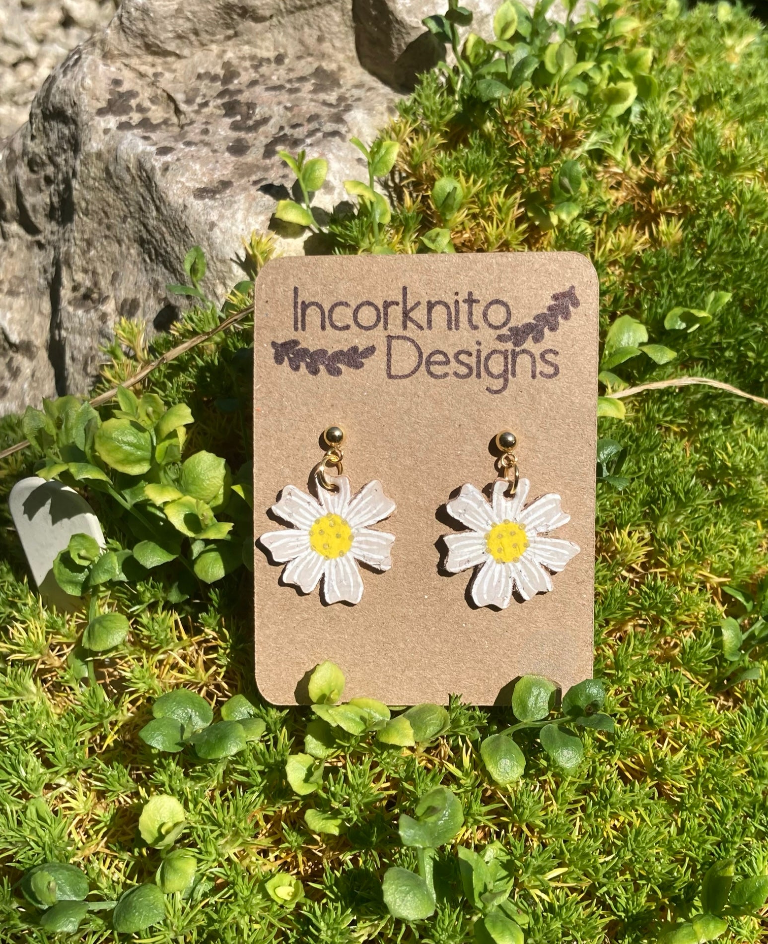 Our handpainted daisy earrings sat on moss in the sun