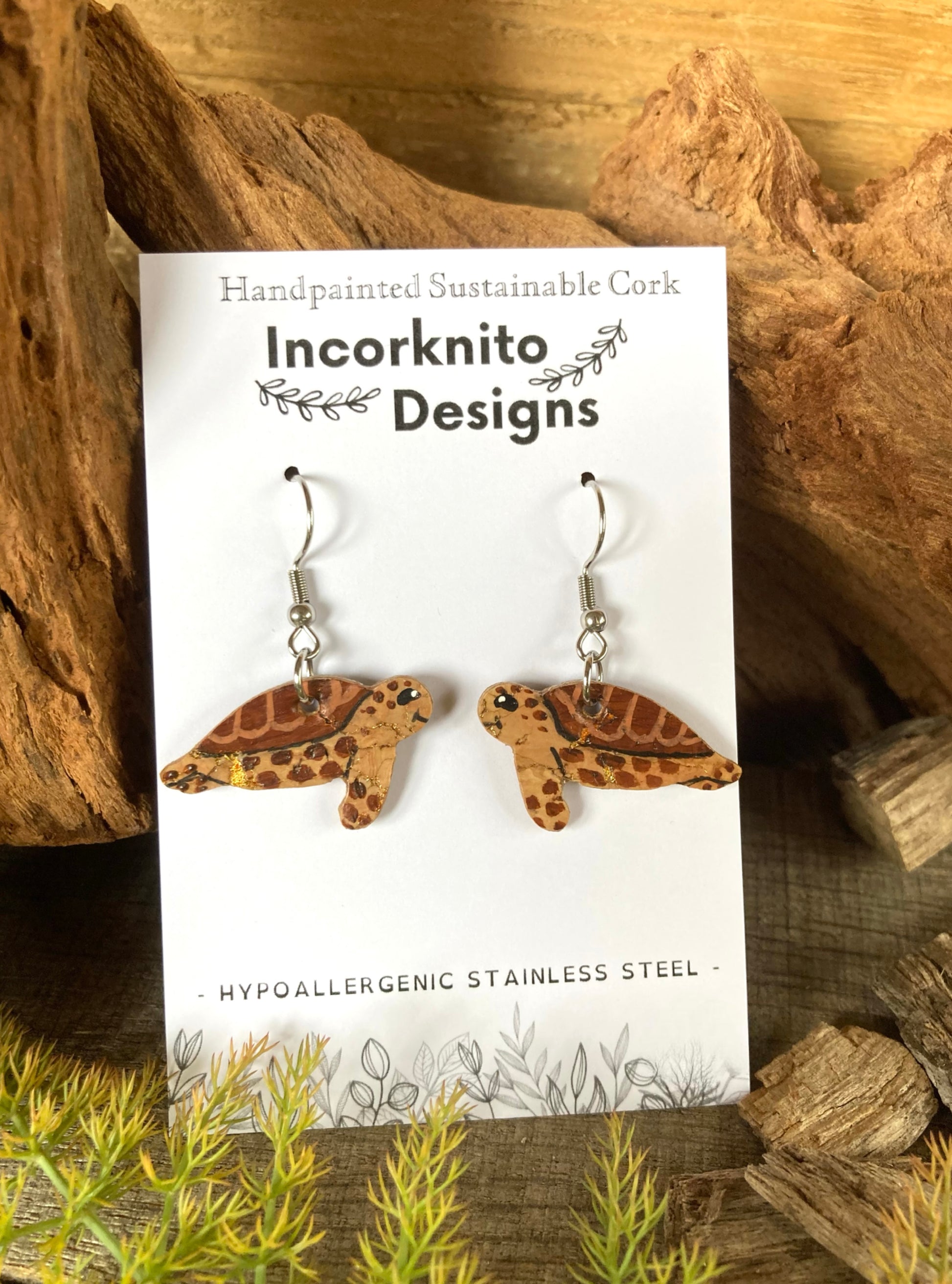 Tortoise-shaped earrings on a card with 'Incorknito Designs' branding, set against a natural wood background.