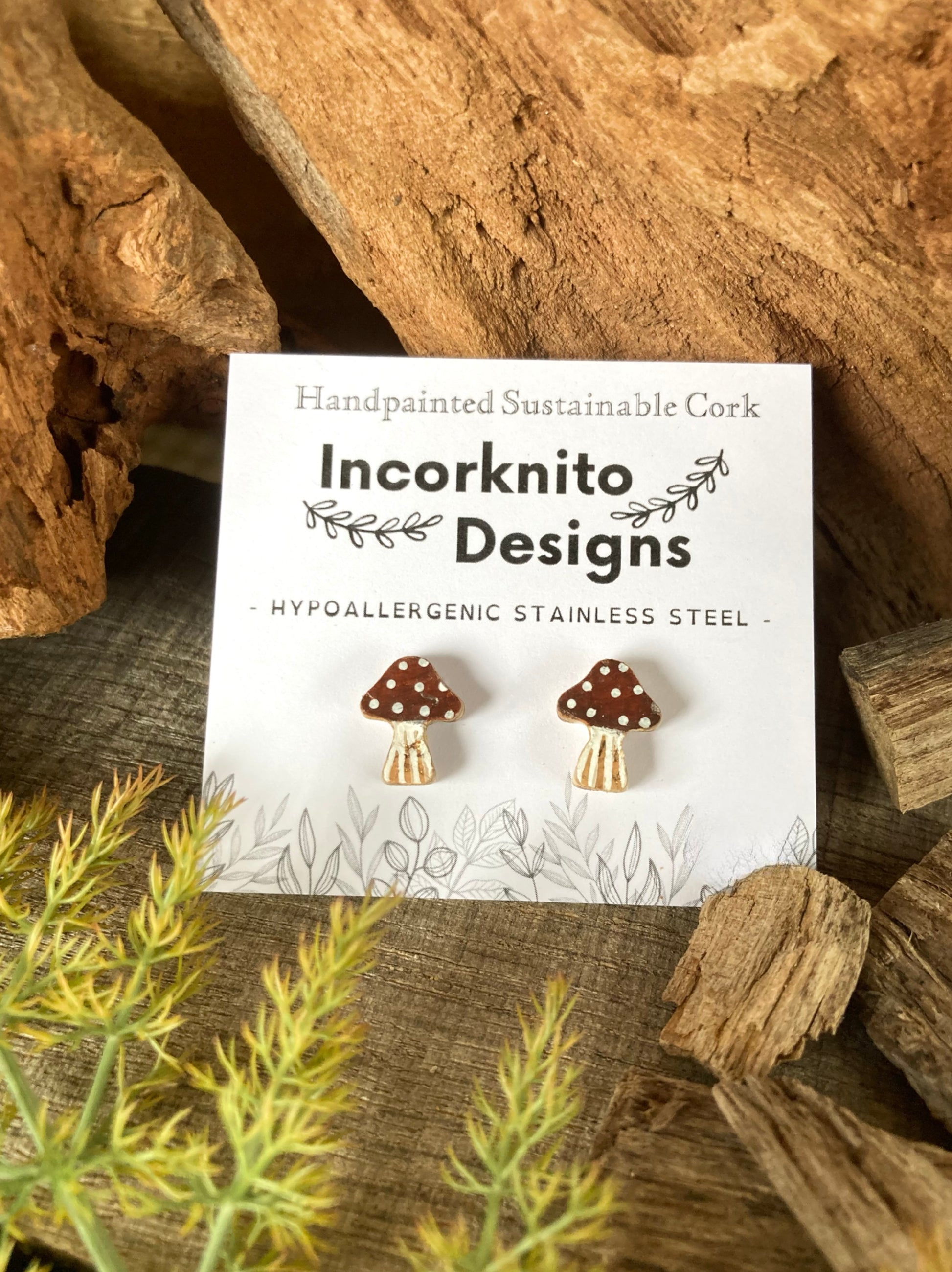 Card with mushroom-shaped earrings on a natural wood background, featuring 'Incorknito Designs'.