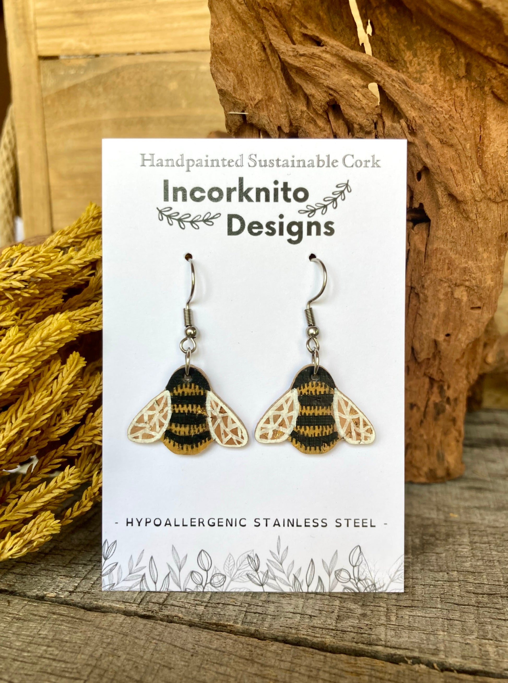 Bee-themed earrings on a card with 'Incorknito Designs' branding, placed on a wooden surface.