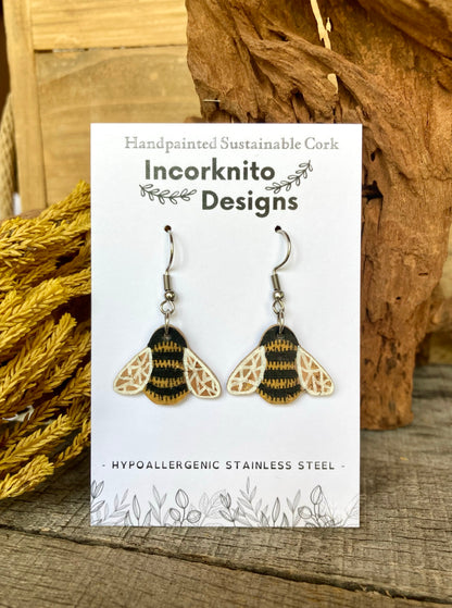 Bee-themed earrings on a card with 'Incorknito Designs' branding, placed on a wooden surface.