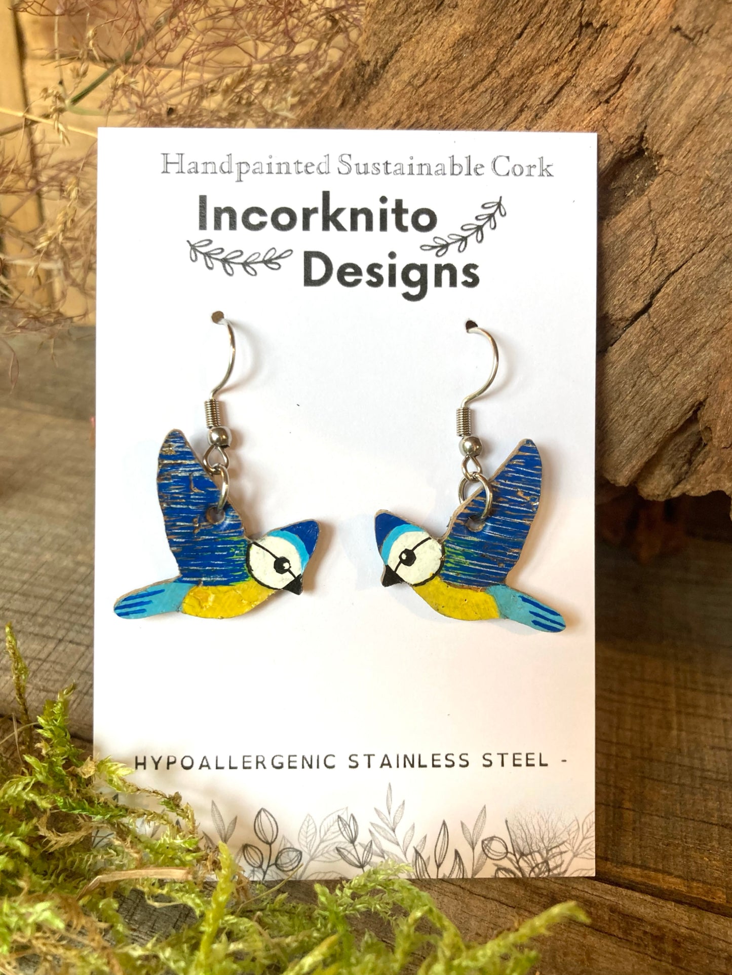 Bird-shaped earrings on a white card with 'Incorknito Designs' branding, set against a wooden background.