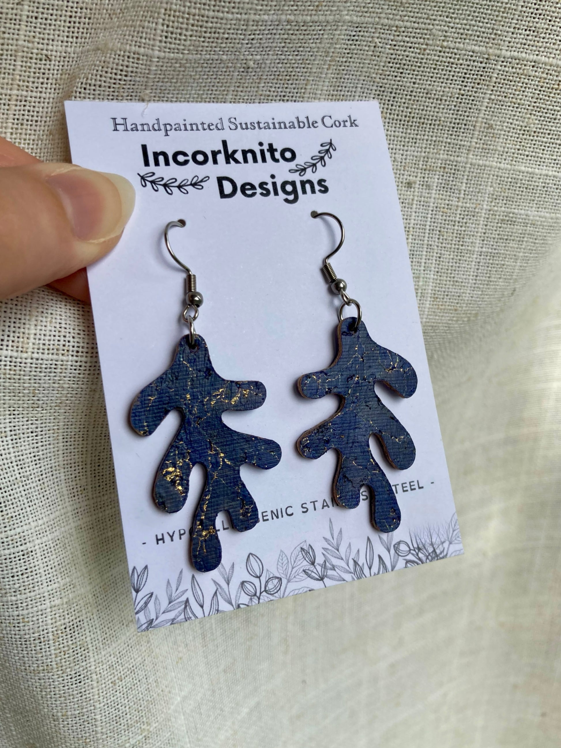 Blue branch shaped earrings on a 'Incorknito Designs' card against a beige fabric background