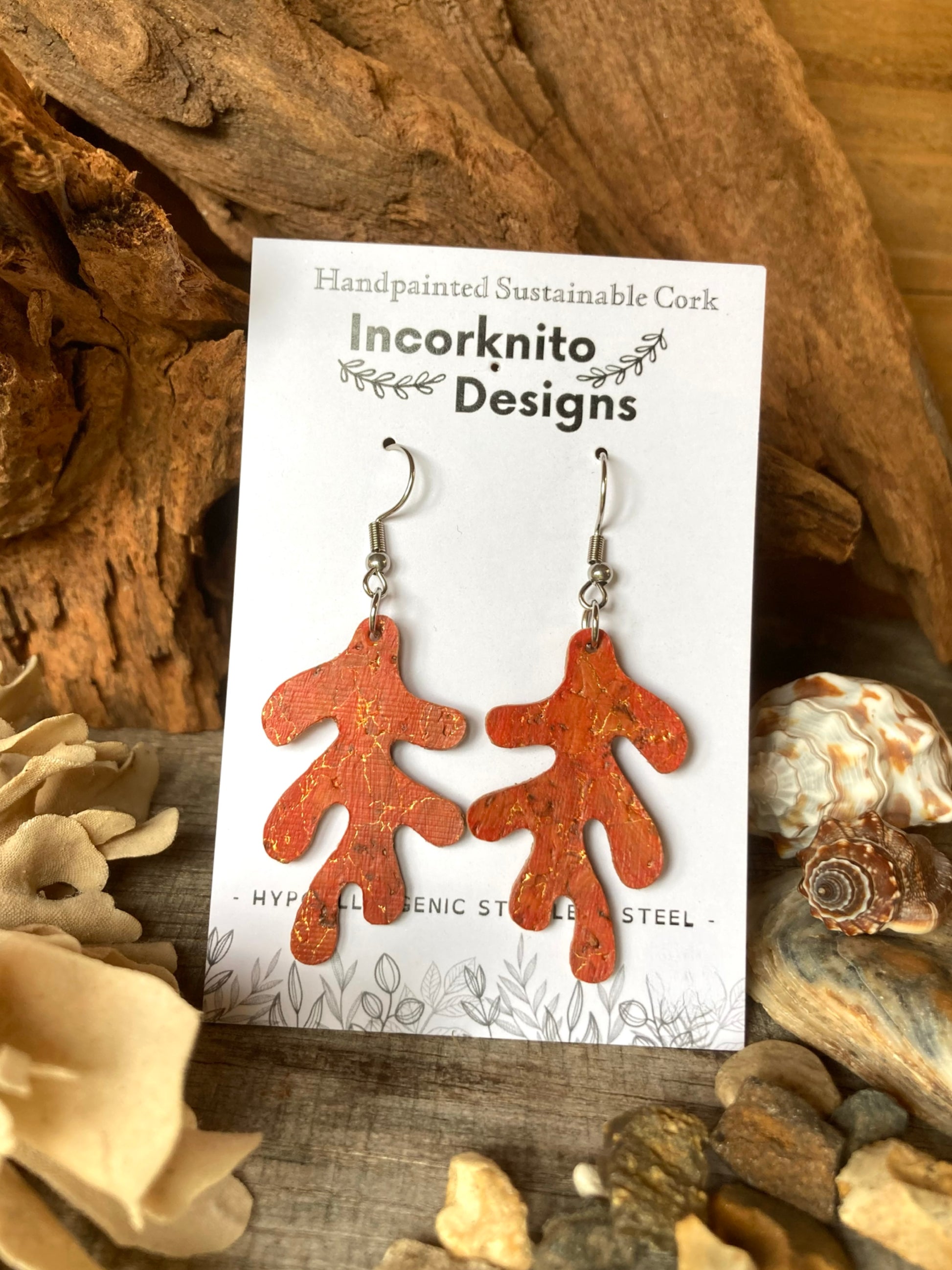 Orange coral shaped earrings on a 'Incorknito Designs' card with natural elements in the background