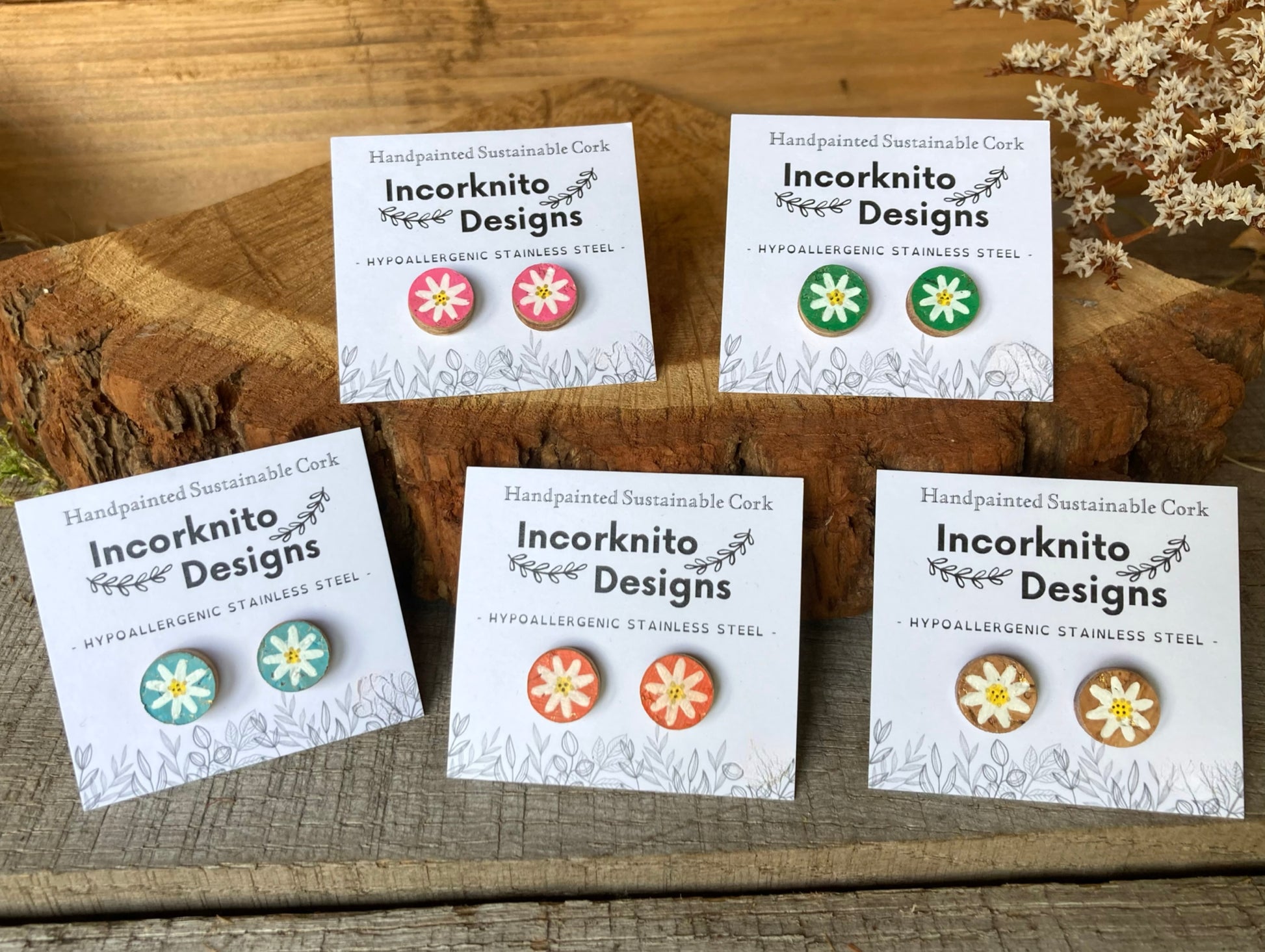 Set of flower-shaped earrings on cards with 'Incorknito Designs' branding, displayed on a wooden surface.