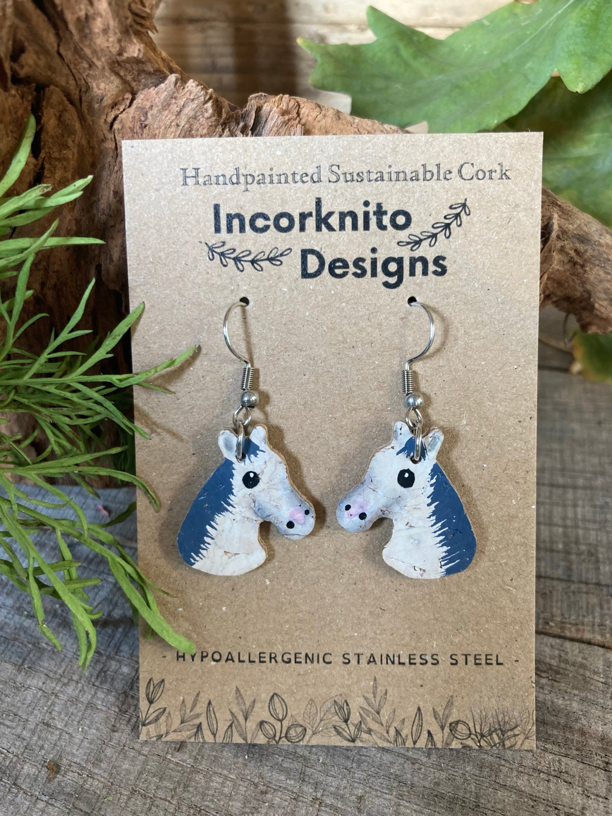 Horse-shaped earrings on a card with 'Incorknito Designs' branding, set against a natural background.