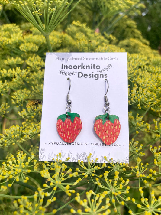 Strawberry-shaped earrings on a card with 'Incorknito Designs' branding, set against a green floral background.