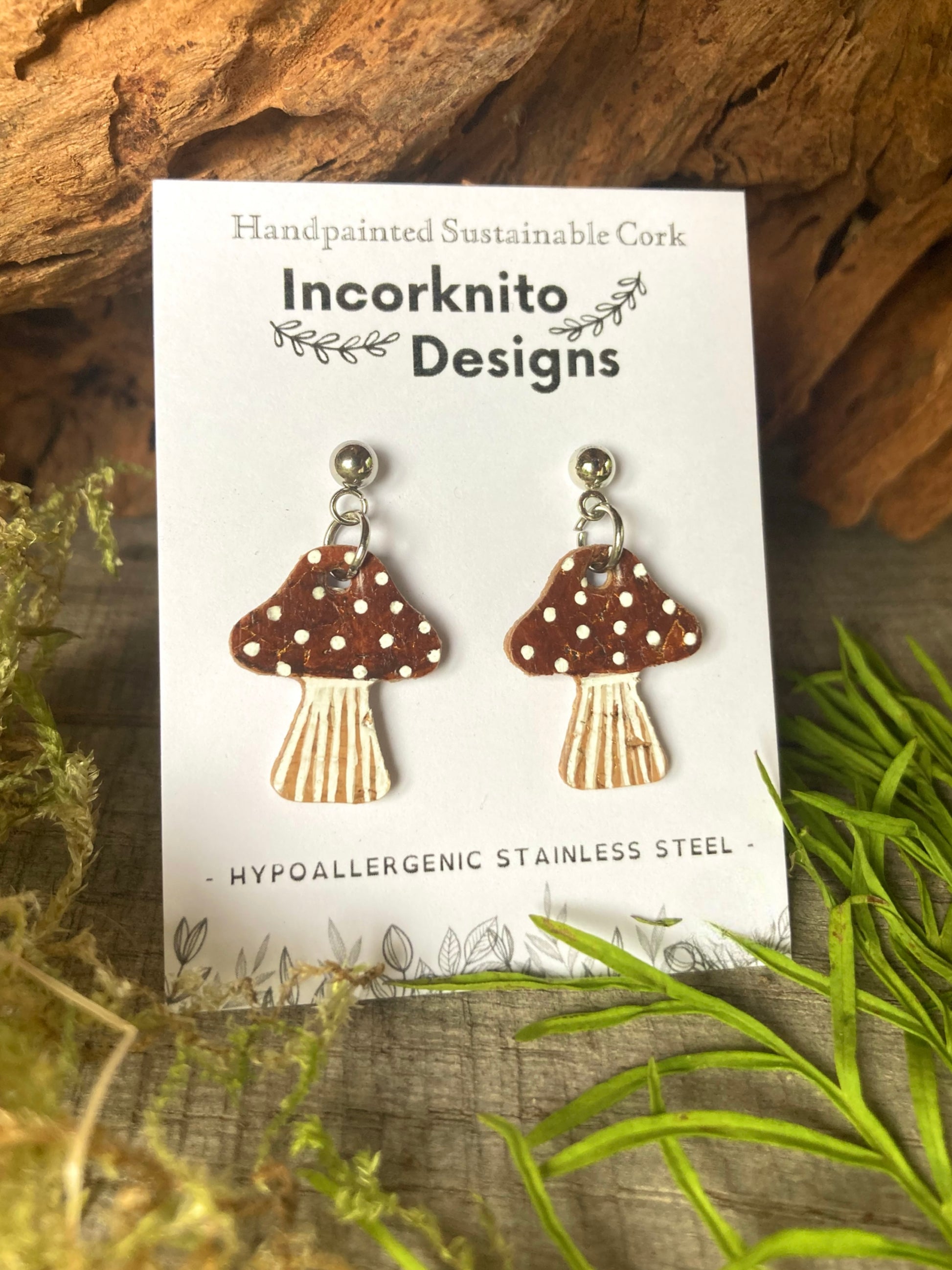 Brown mushroom-shaped earrings on a card with 'Incorknito Designs' branding, set against a natural background.