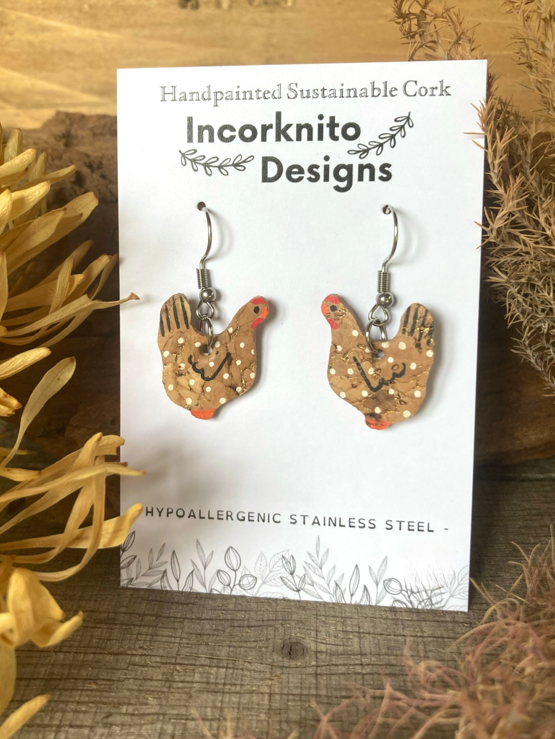 Handmade cork chicken earrings on a 'Incorknito Designs' card with natural elements around.