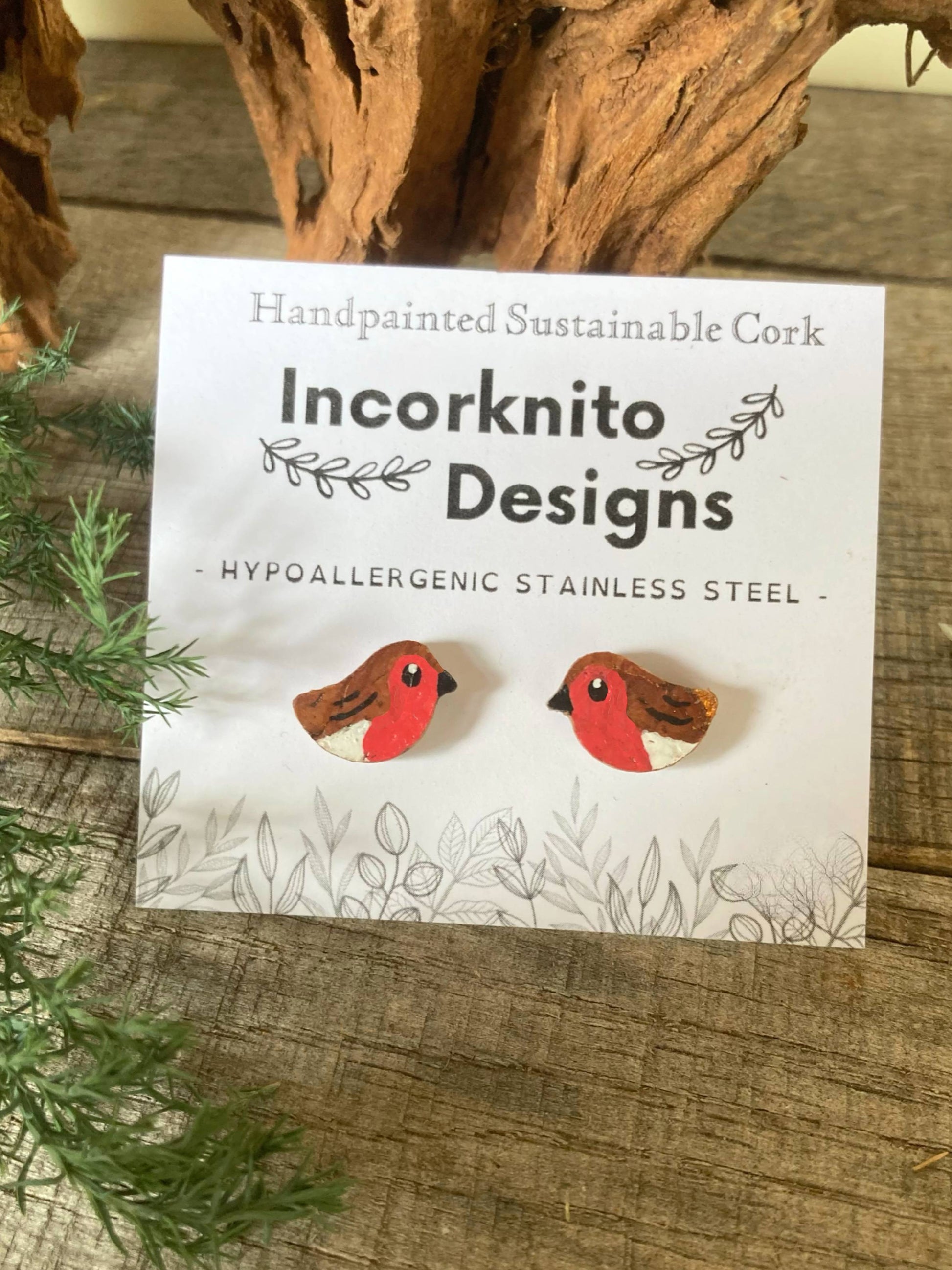Bird-shaped earrings on a card with 'Incorknito Designs' branding, placed on a wooden surface.