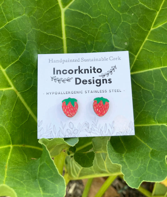 Strawberry earrings on a white card with 'Incorknito Designs' branding, set against a green leafy background.
