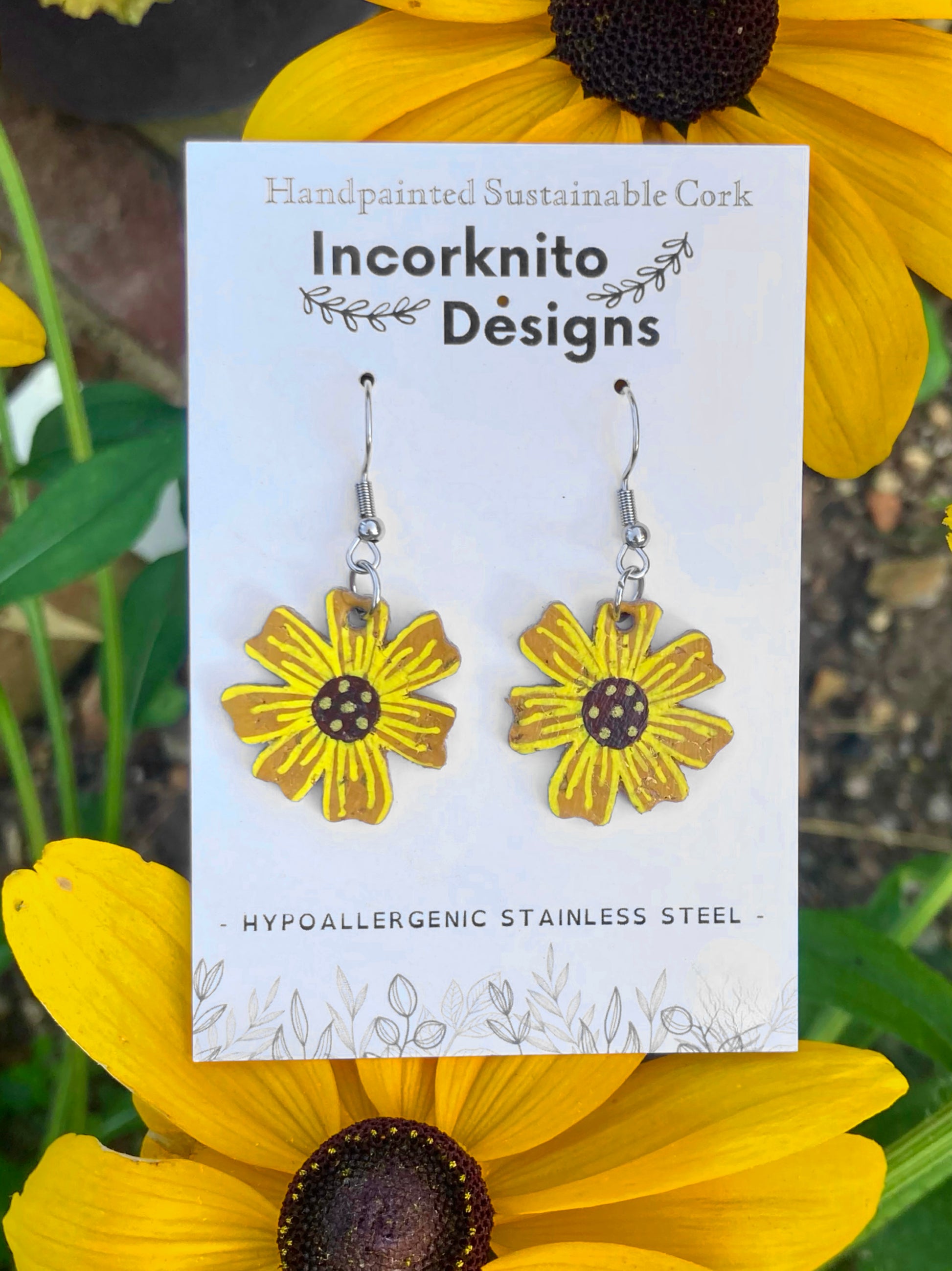Sunflower-shaped earrings on a card with 'Incorknito Designs' branding, surrounded by yellow flowers.