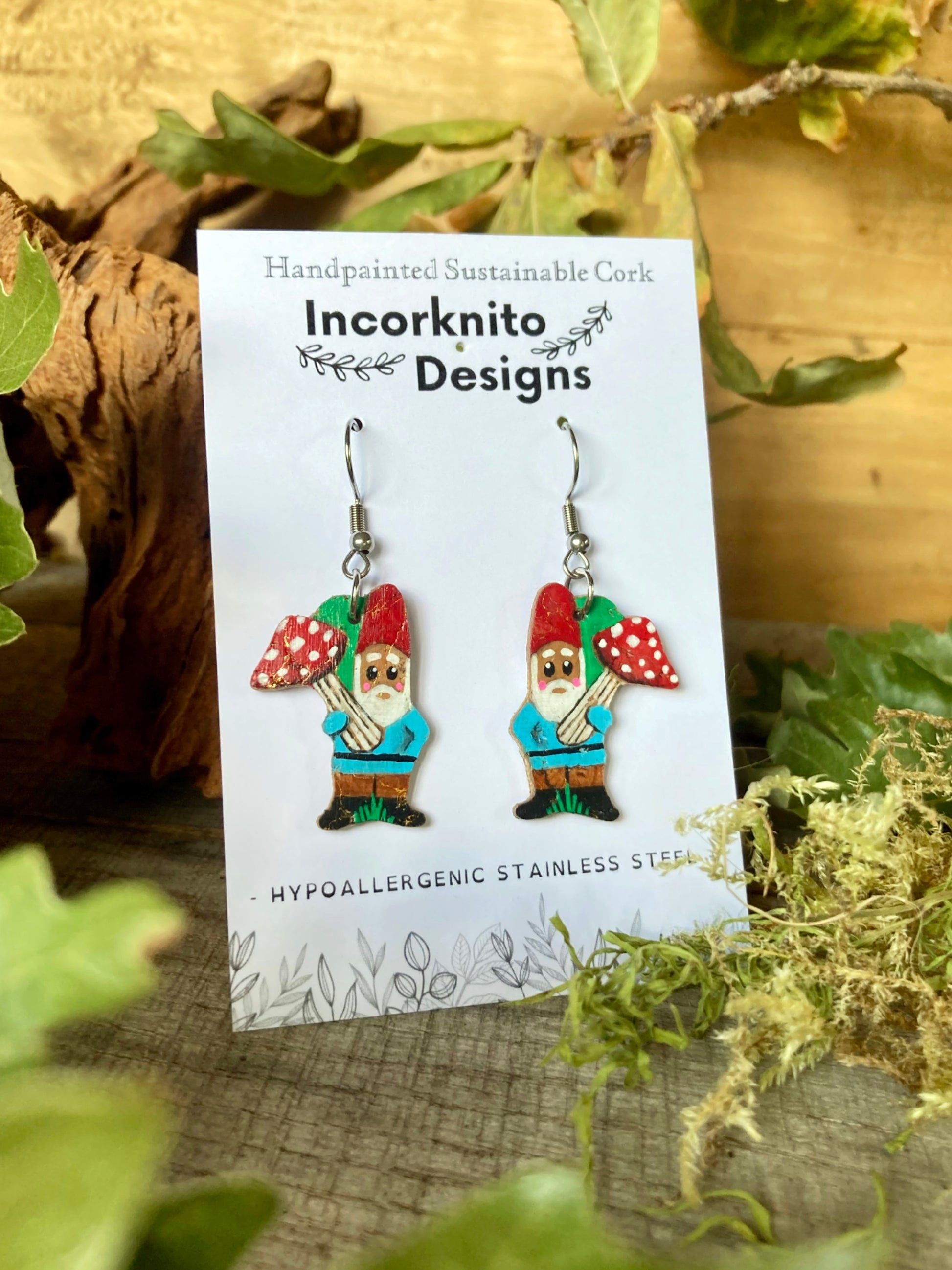 Gnome-themed earrings on a 'Incorkinito Designs' card with greenery in the background
