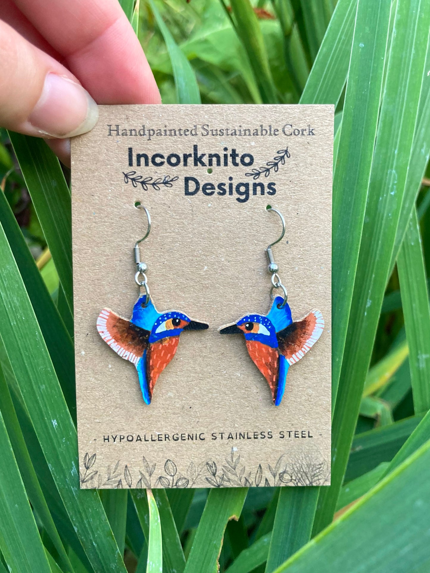 Bird-shaped earrings on a Incorknito Designs card with green grass background