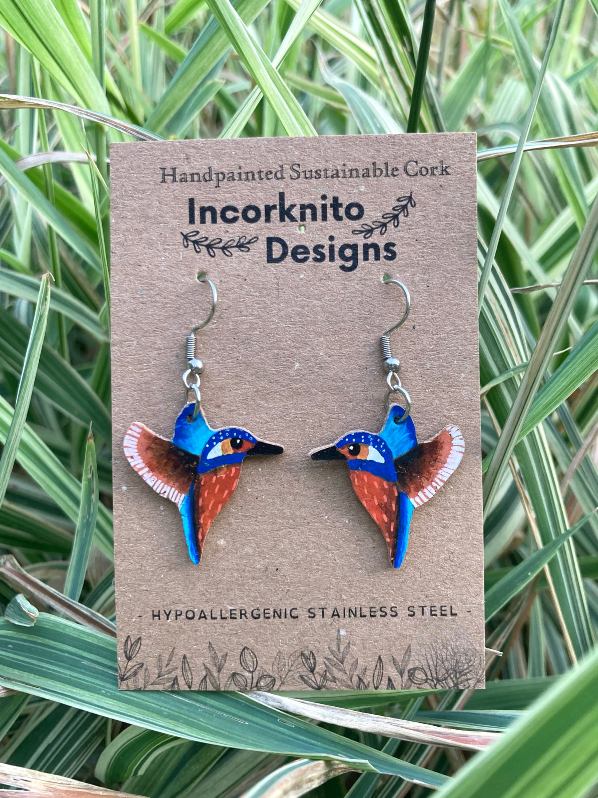 Kingfisher-shaped earrings on a card with 'Incorknito Designs' branding, set against a natural background.