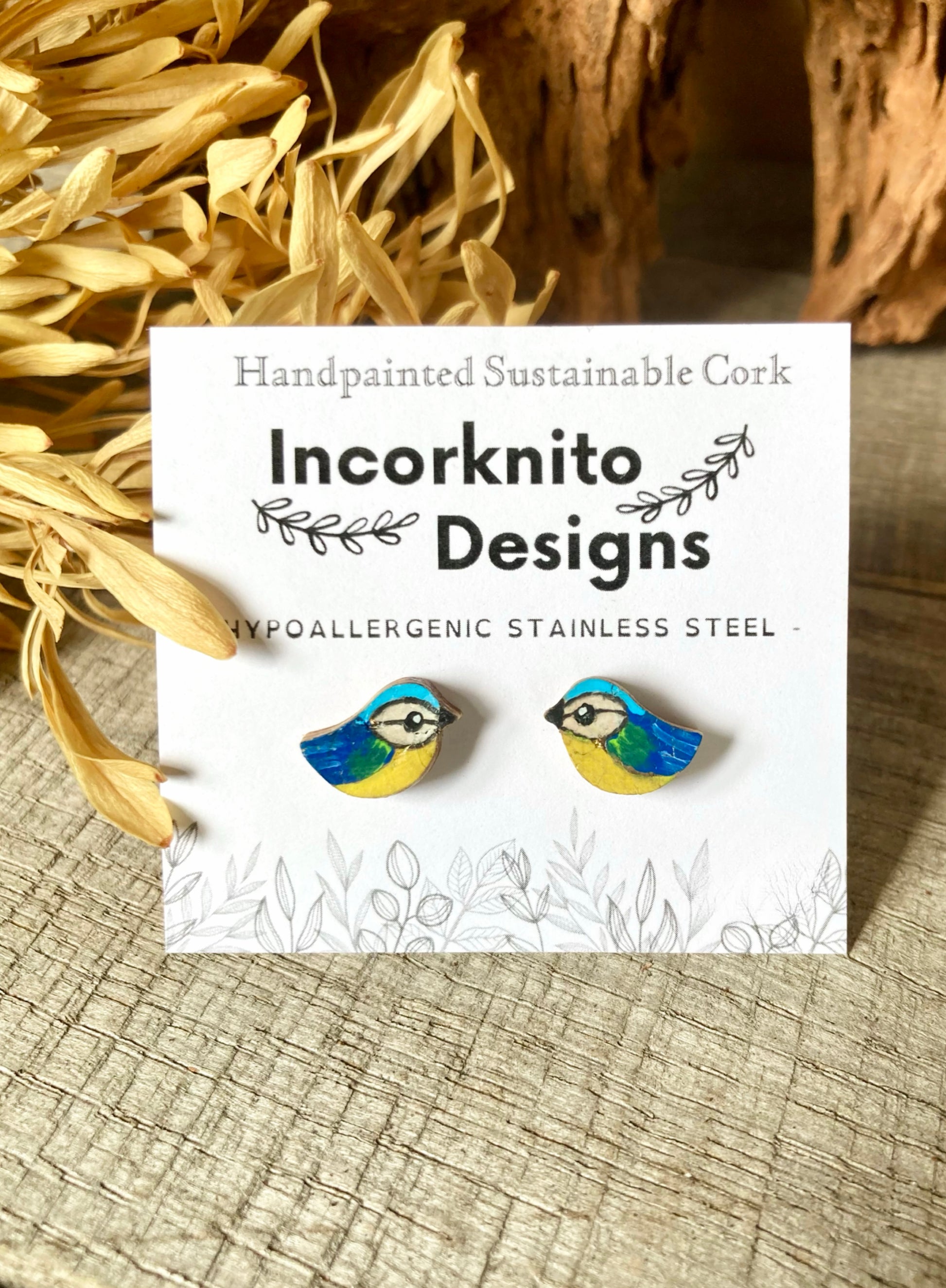 Blue tit earrings on a cork background with 'Incorknito Designs' label