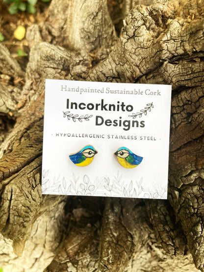 Yellow and blue bird earrings on a label with 'Incorknito Designs' text, placed on a wooden surface.