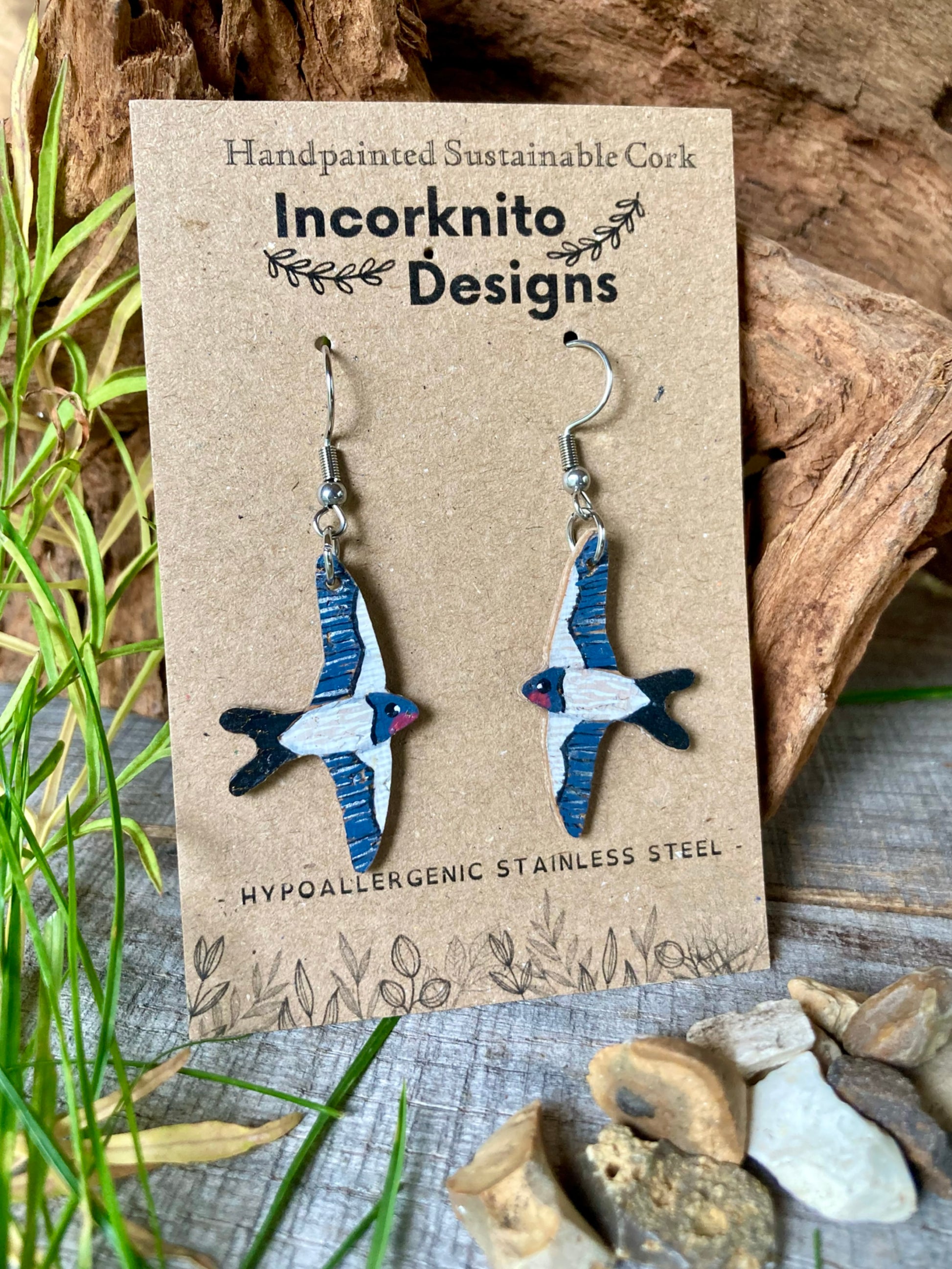 Pair of bird-shaped earrings on a 'Incorknito Designs' card with natural elements in the background.