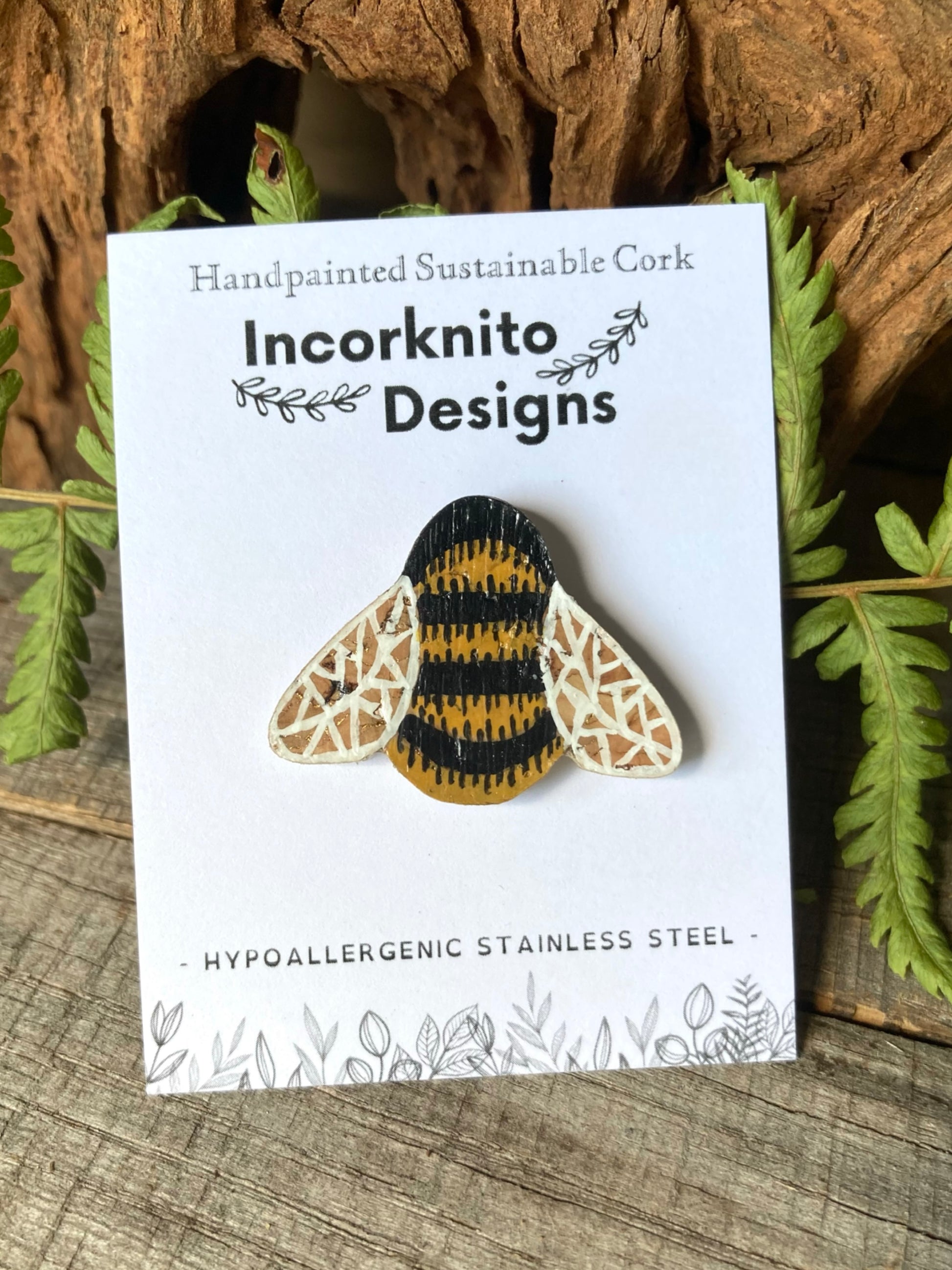 Incorknito Designs cork bee brooch on a white card with green leaves in the background
