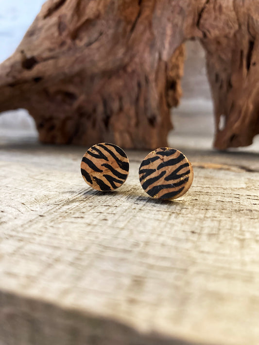A pair of tiger print stud earrings made from cork leather with gold flecks, displayed on a wooden surface.