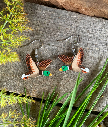 Duck-shaped earrings on a wooden surface with greenery around