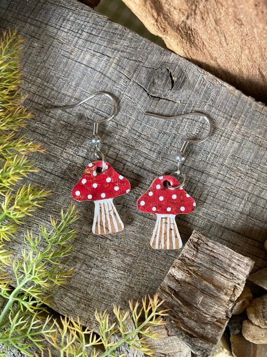 Mushroom-shaped earrings with red caps and white spots on a wooden surface.